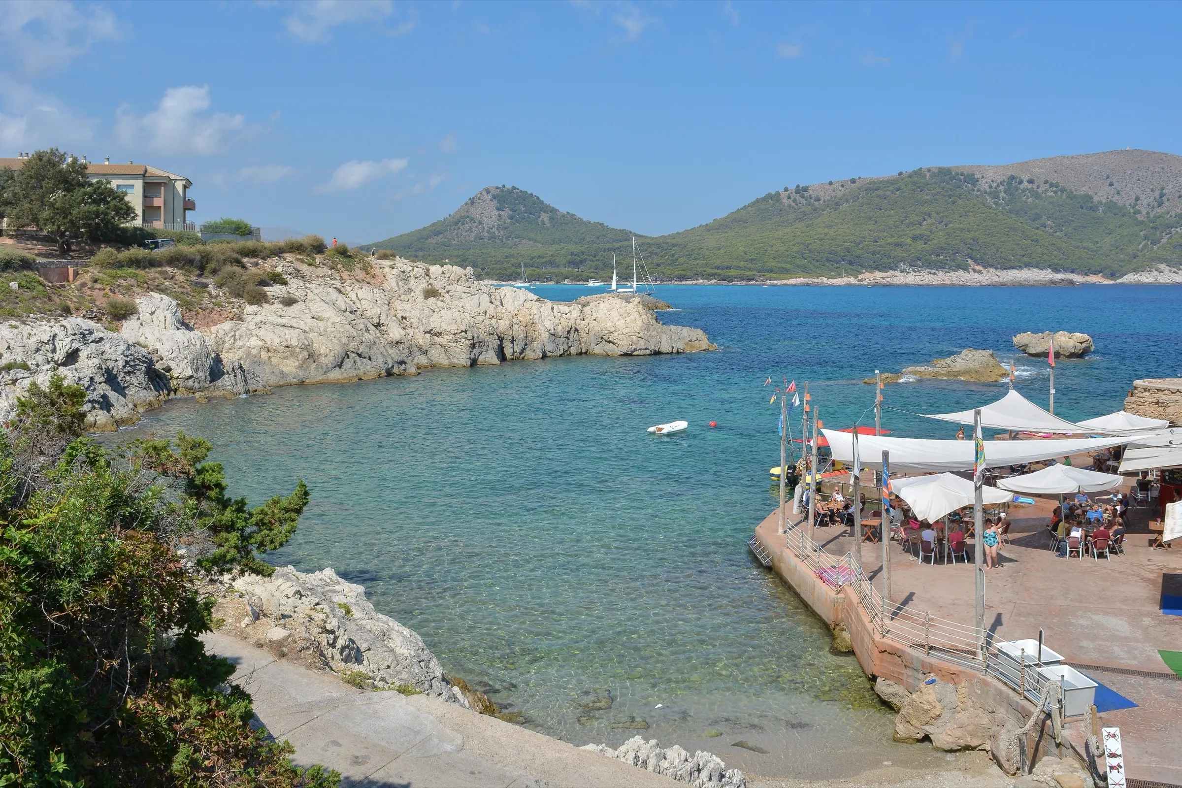 Cala Lliteres from above, with turquoise water, the platform with the bar terrace and the mountain behind