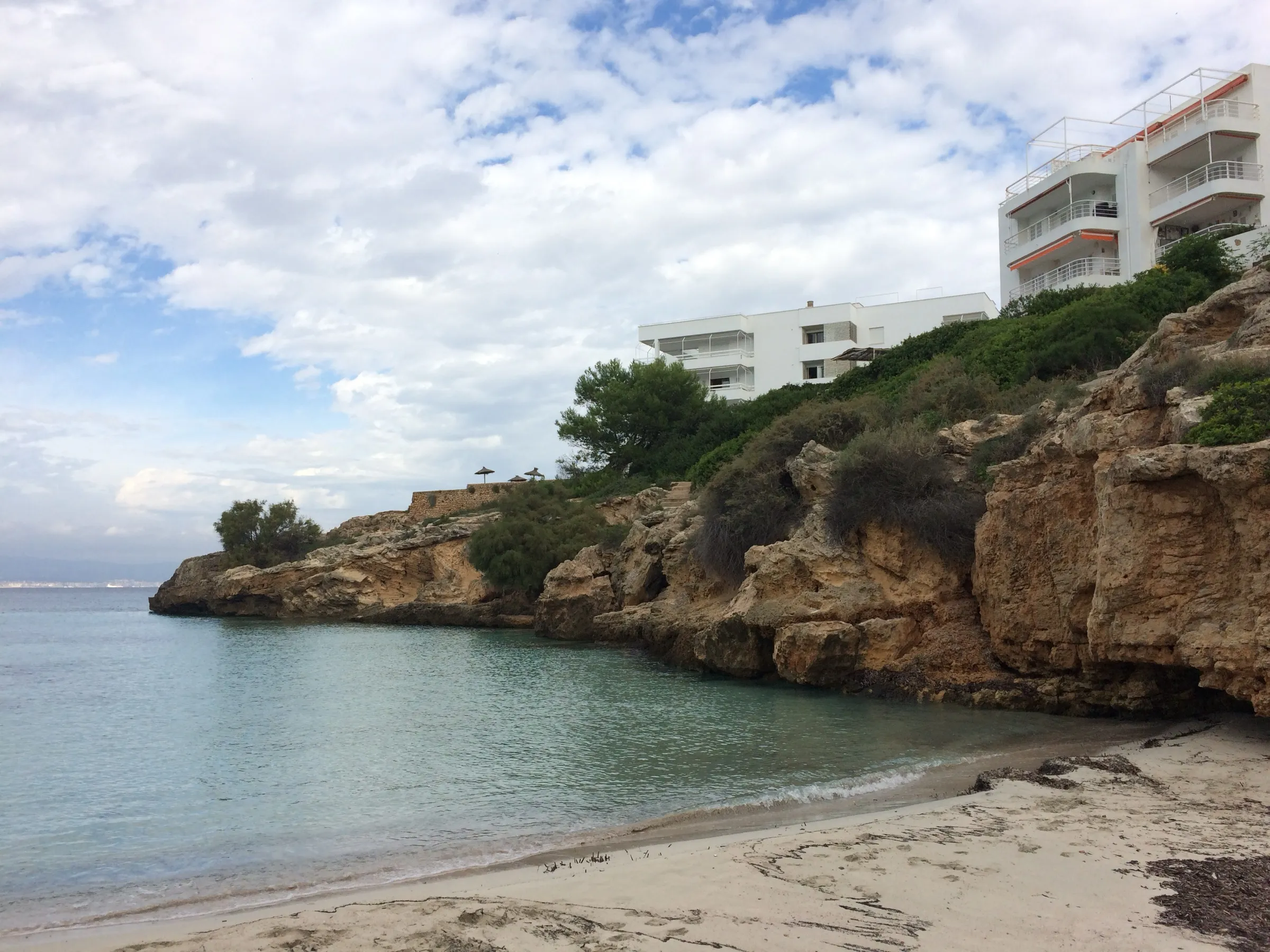 The sand of Cala Blava between low cliffs, with clear water and the estate's houses above