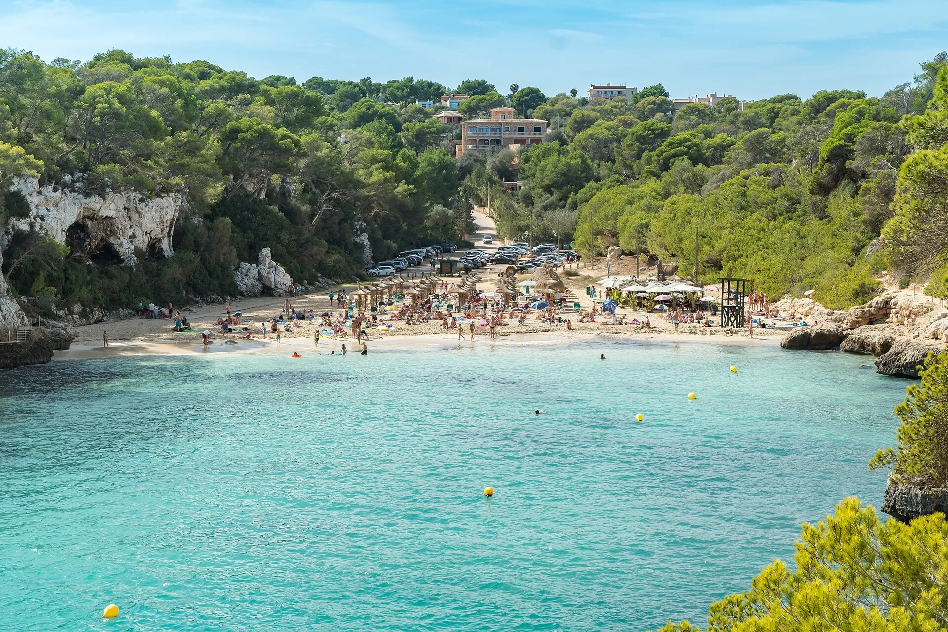Vista de Cala Llombards desde el agua, con la playa de arena blanca al fondo entre rocas y pinar