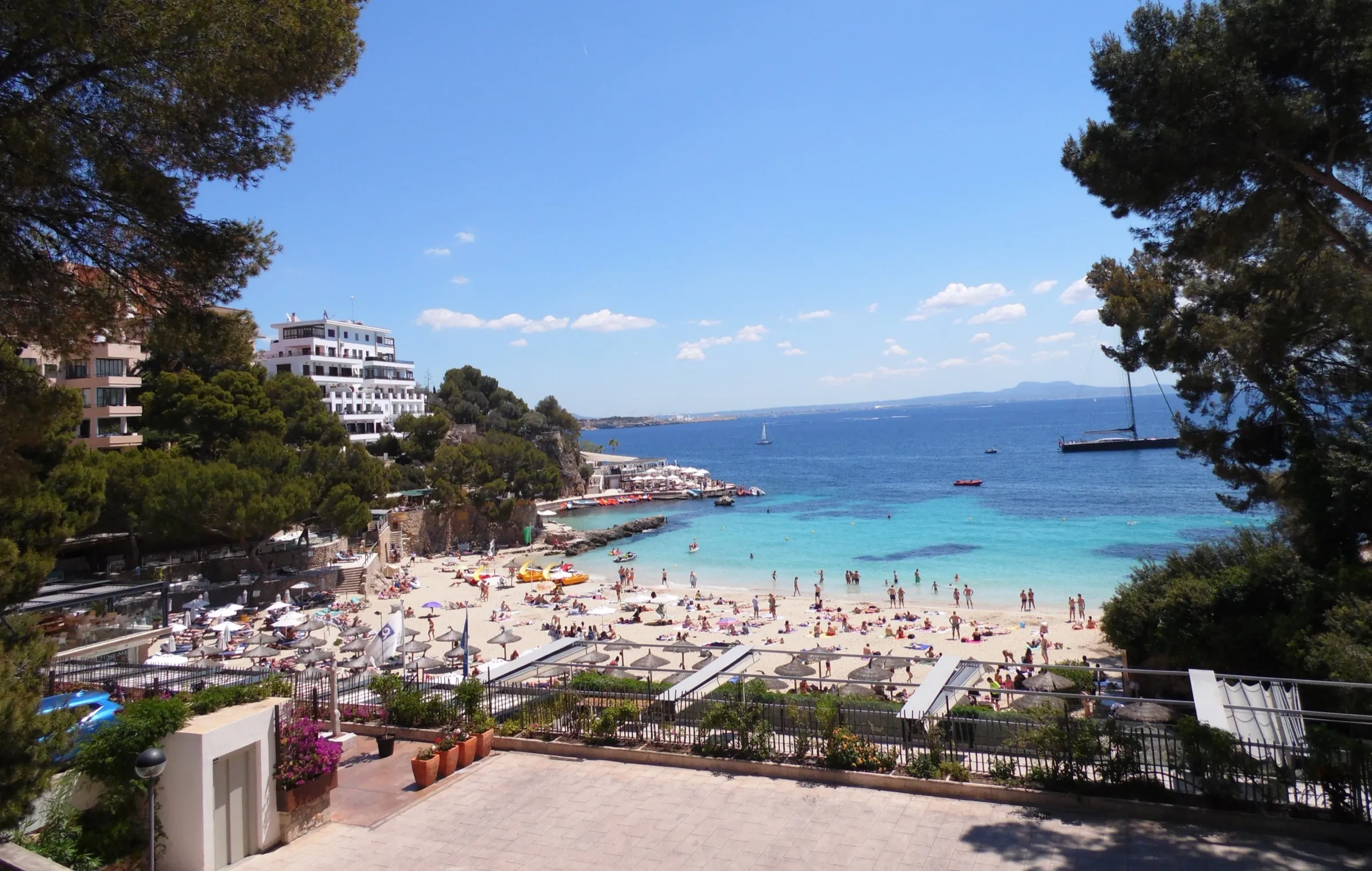 La Platja de ses Illetes vista desde las terrazas de arriba, con la arena llena de gente y el agua turquesa