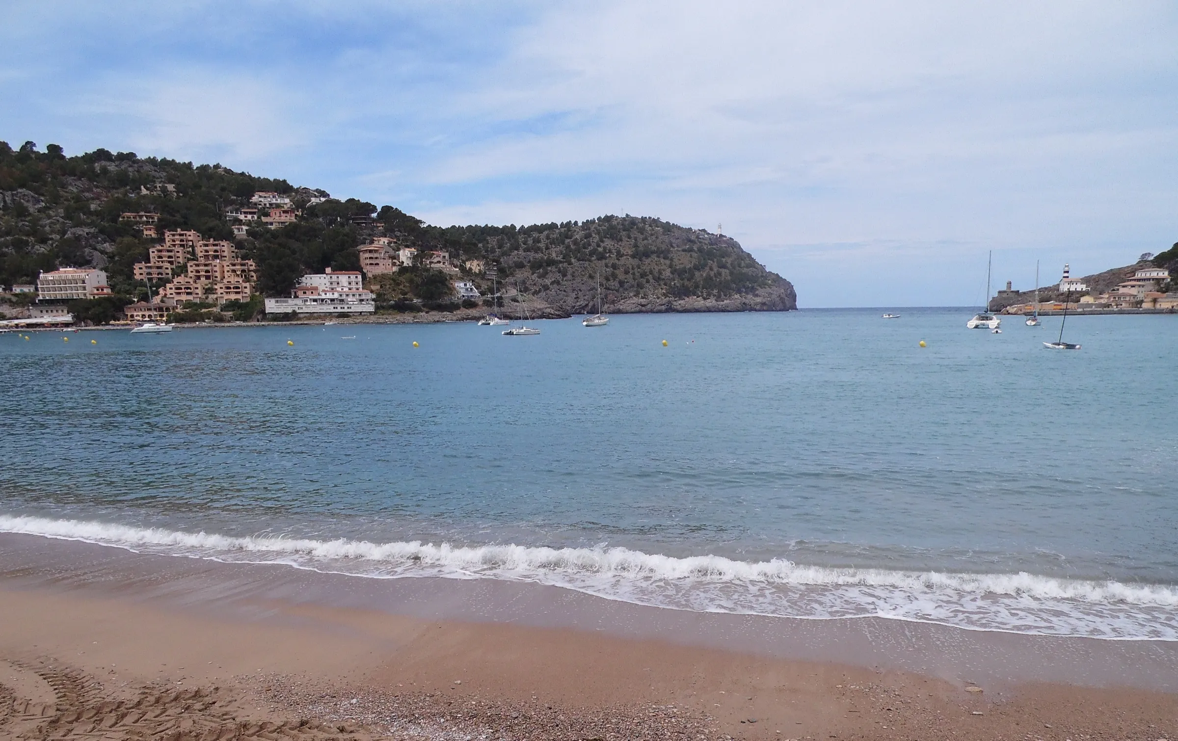La orilla de arena de Platja d'en Repic con la bahía del Port de Sóller delante y la boca del puerto al fondo entre dos cabos