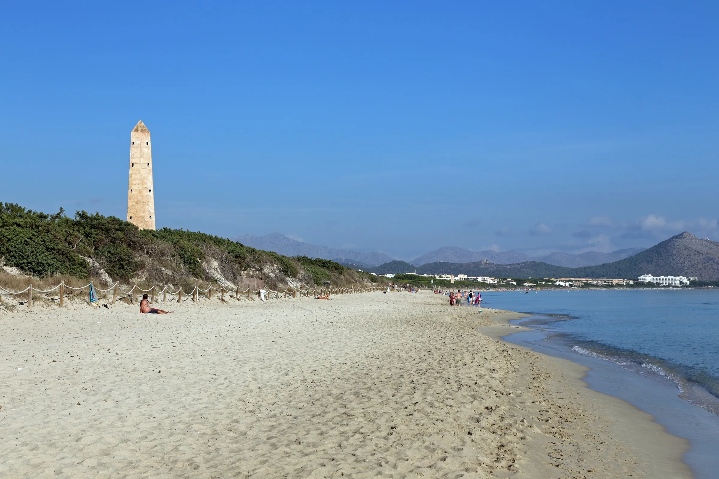 Arena clara de Es Comú con la torre de enfilación sobre las dunas y la bahía de Alcúdia al fondo