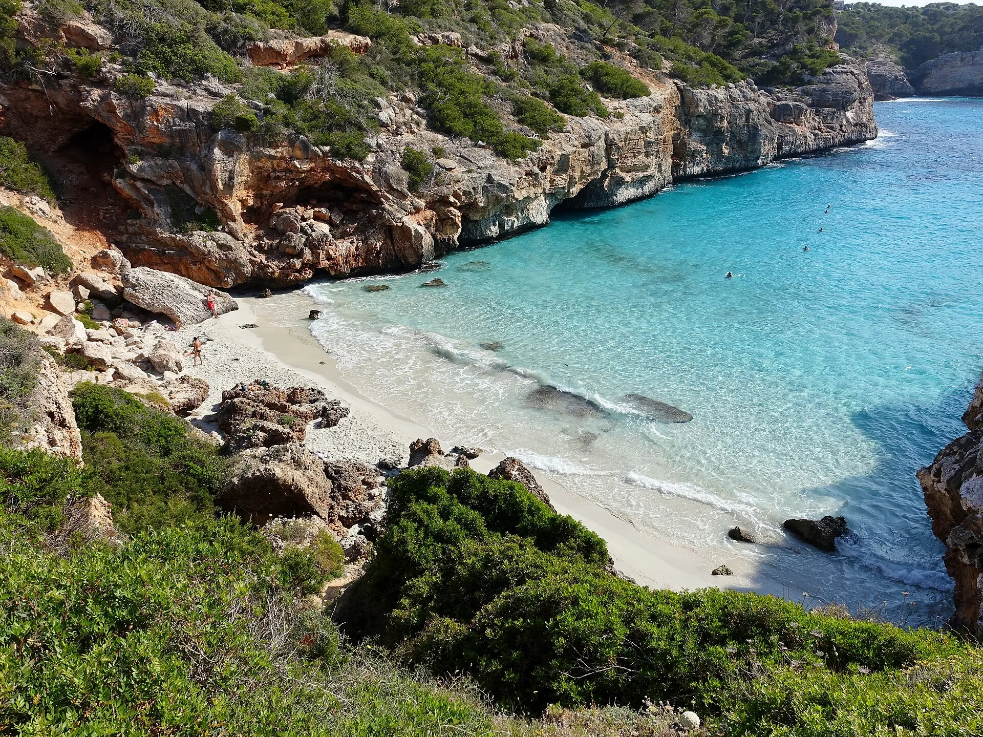 Vista desde lo alto del Caló des Moro, con la playa de arena blanca, el agua turquesa y las paredes de roca con pinos abriéndose al mar