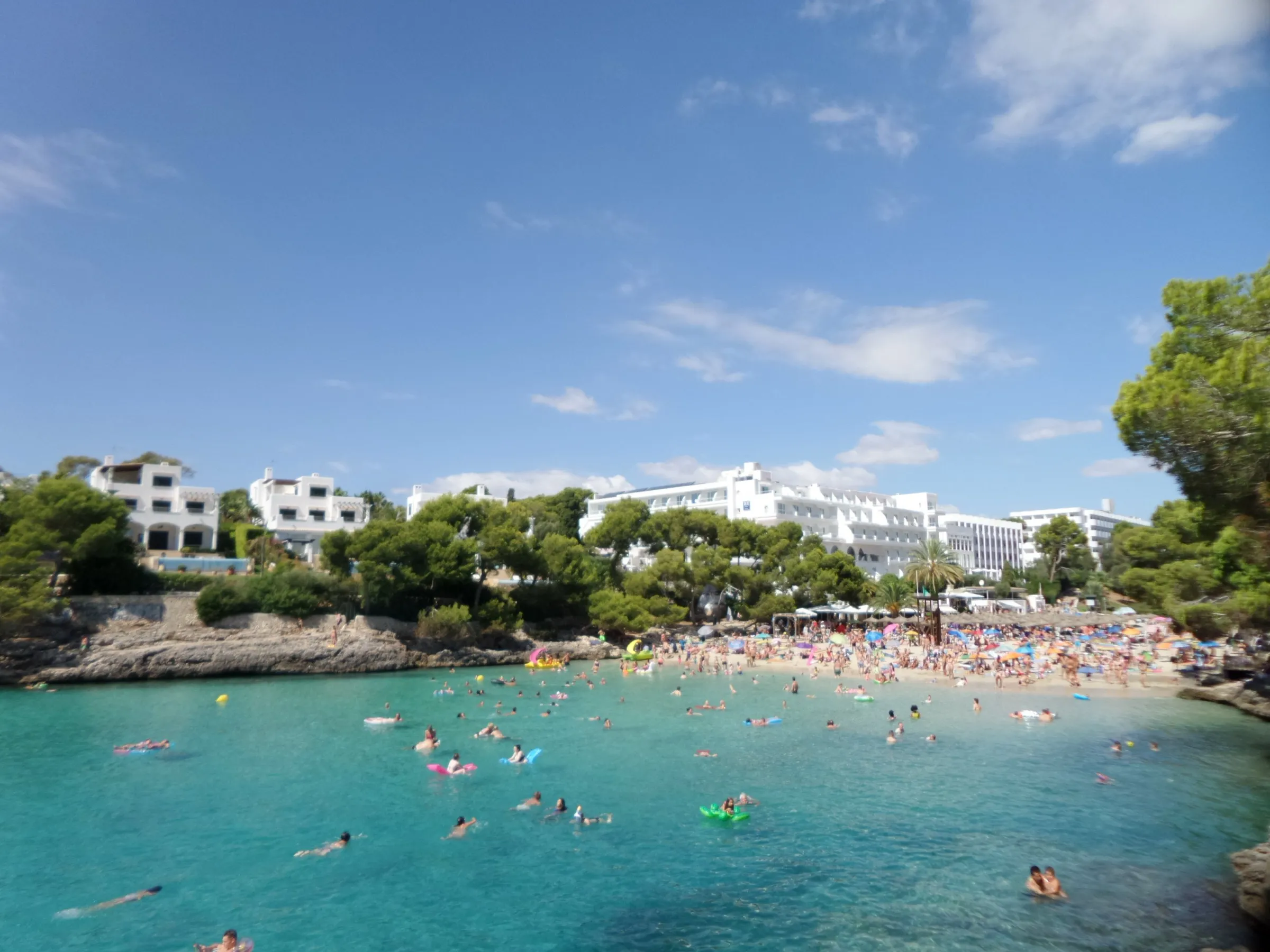 Cala Gran from the rocks, with turquoise water full of swimmers, the sand behind and hotels among the pines