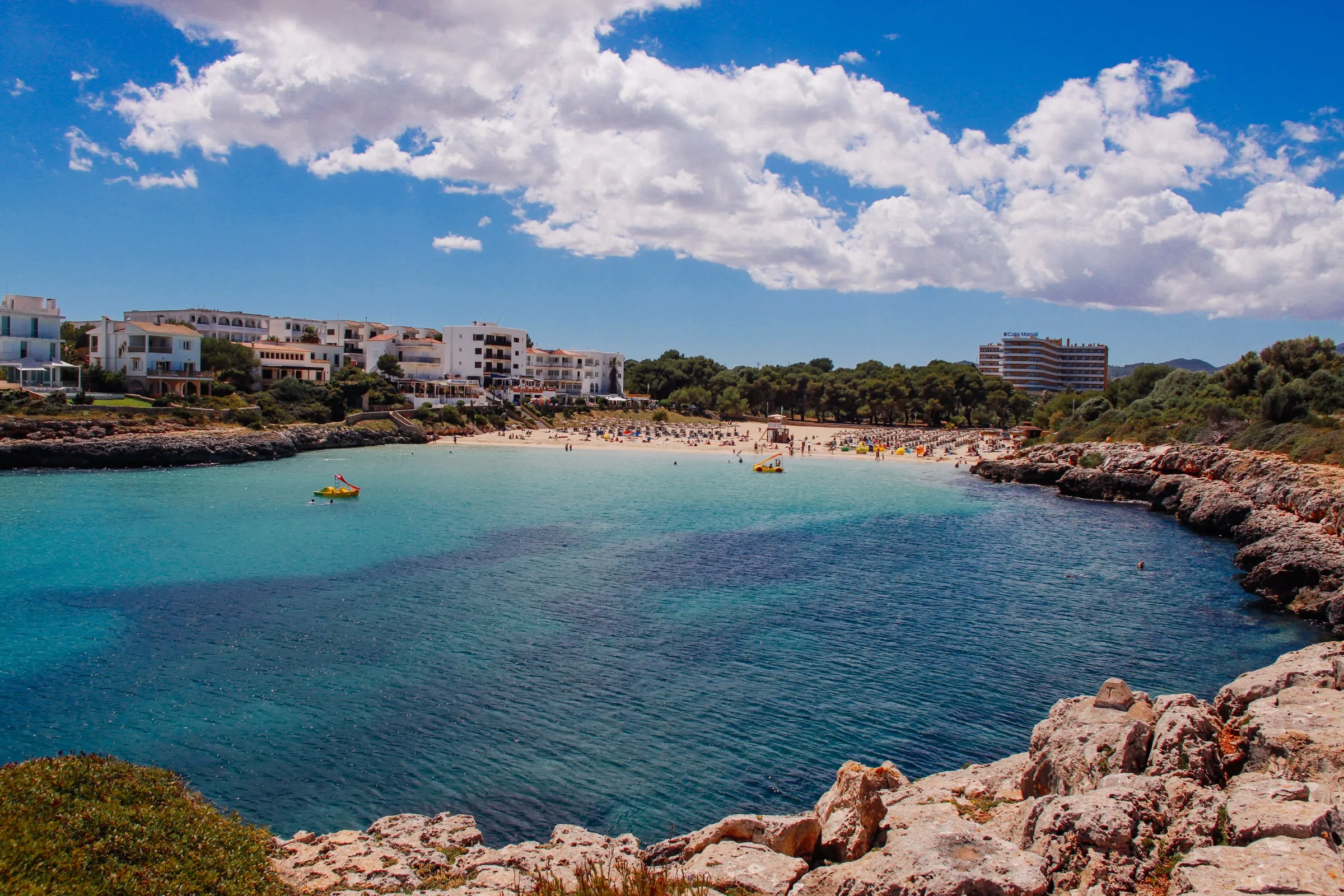 Cala Marçal desde las rocas del lateral, con el agua turquesa, la playa de arena al fondo y los hoteles detrás