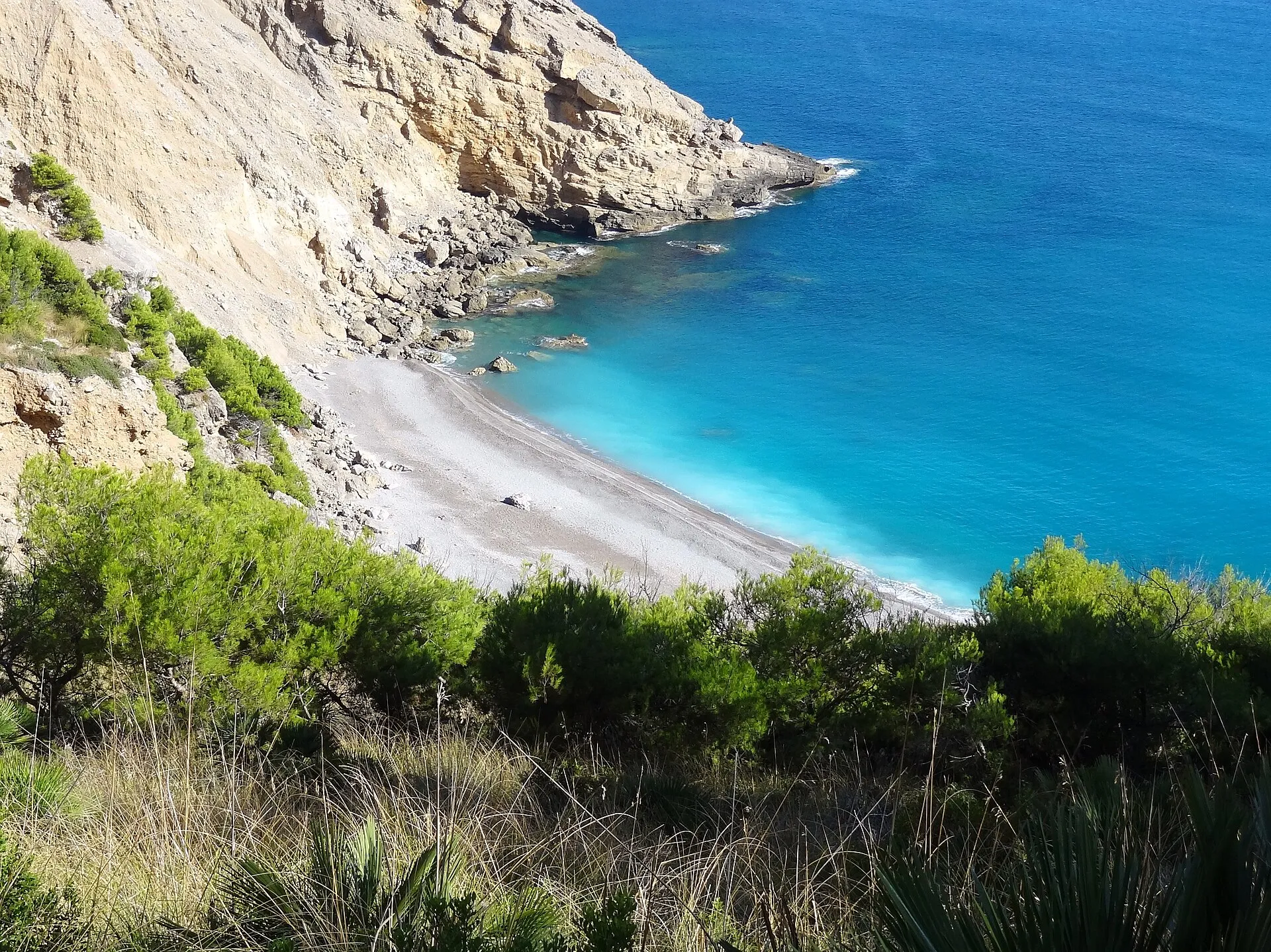 Vista desde el sendero de la playa de canto rodado de es Coll Baix, con el agua turquesa bajo el acantilado