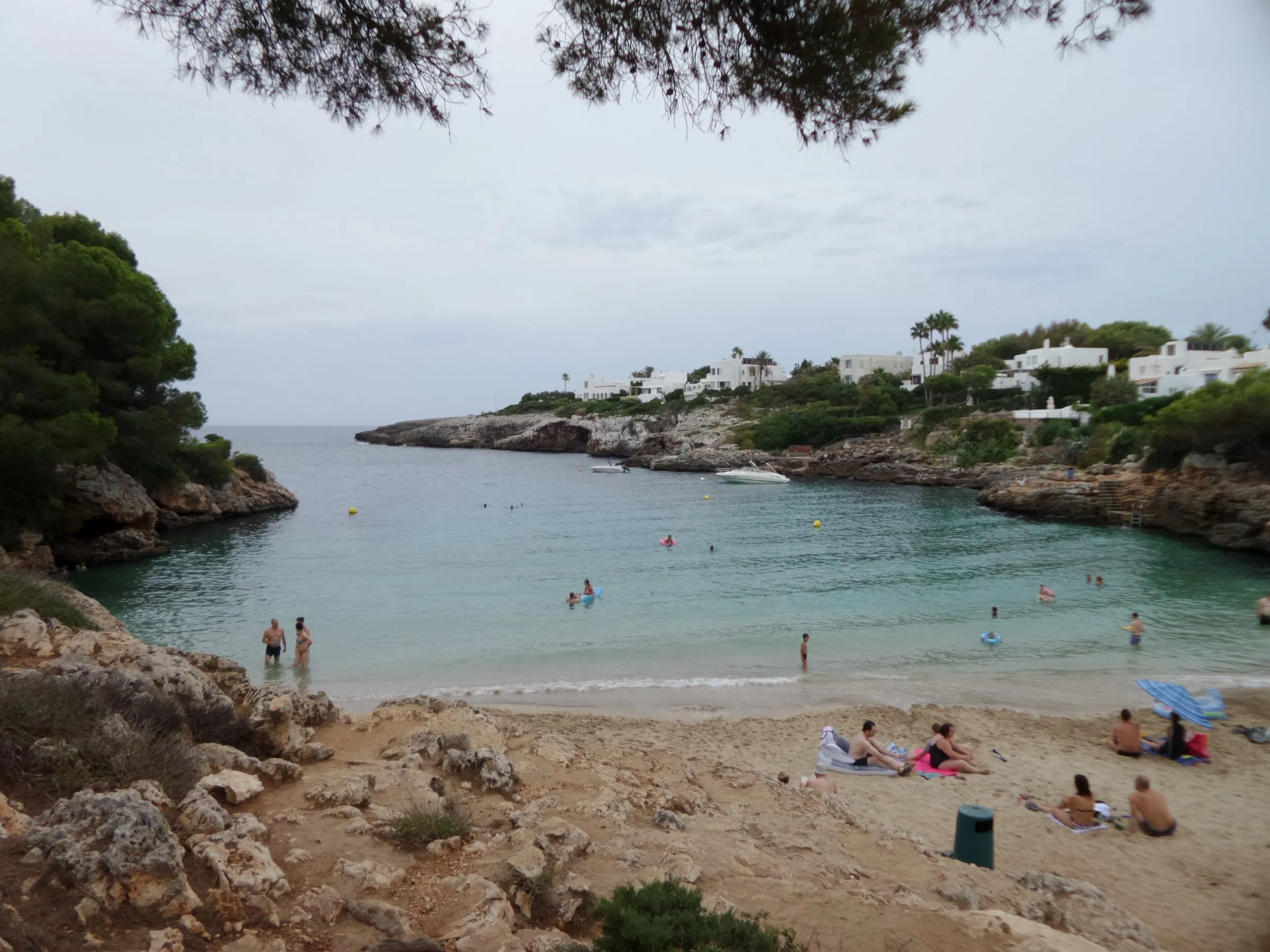 Cala Esmeralda desde el borde de la arena, con el agua verde y transparente, bañistas y la boca de la cala entre rocas y casas blancas