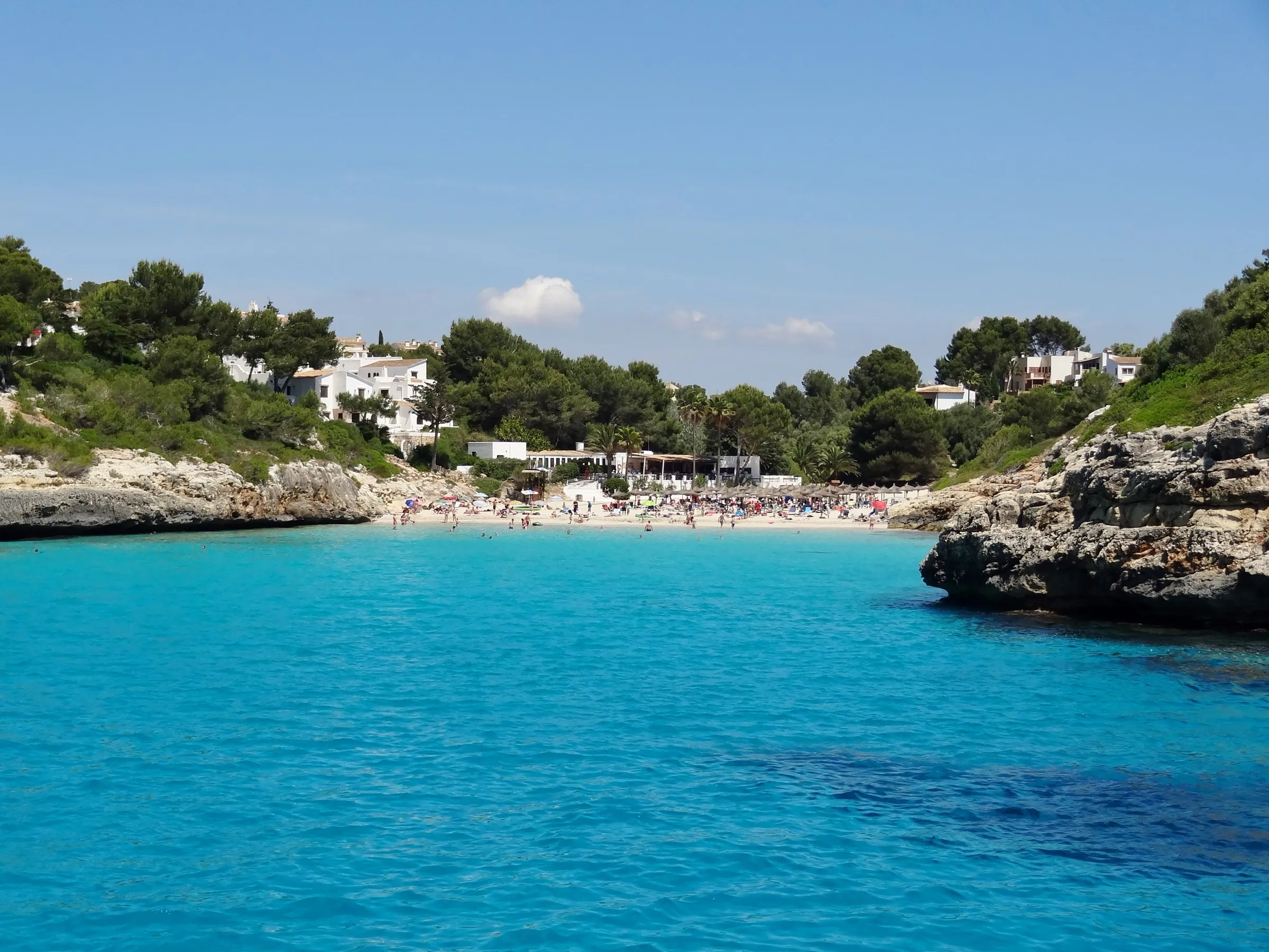 Cala Anguila desde el agua, con el entrante turquesa entre rocas y la playa al fondo bajo los pinos