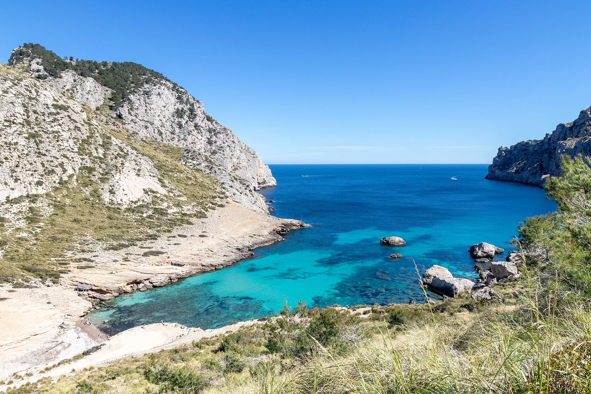 Vista desde la ladera de Cala Figuera, con la playa de cantos, el agua turquesa y la boca abierta al mar entre acantilados