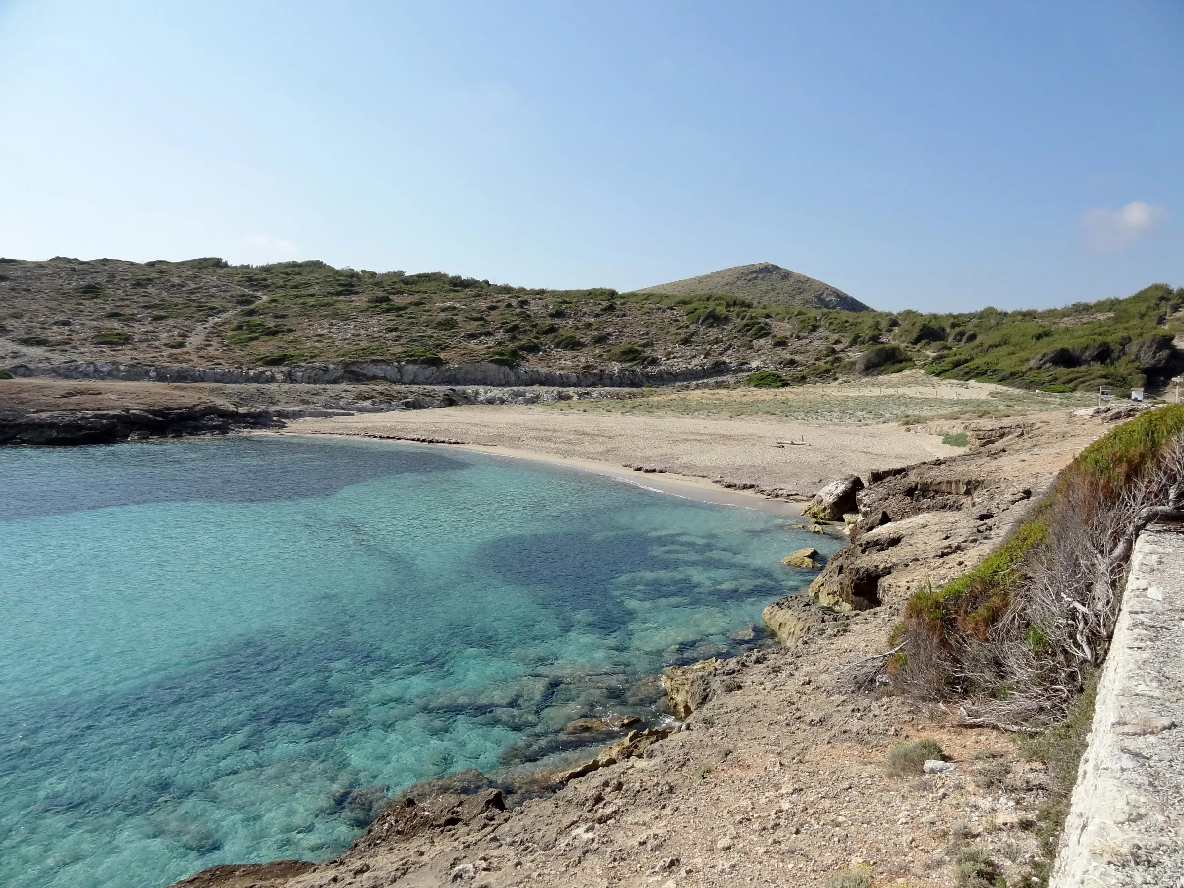 Cala Mitjana desde las rocas del lado este, con el agua turquesa, la playa de arena y los montes bajos de Artà