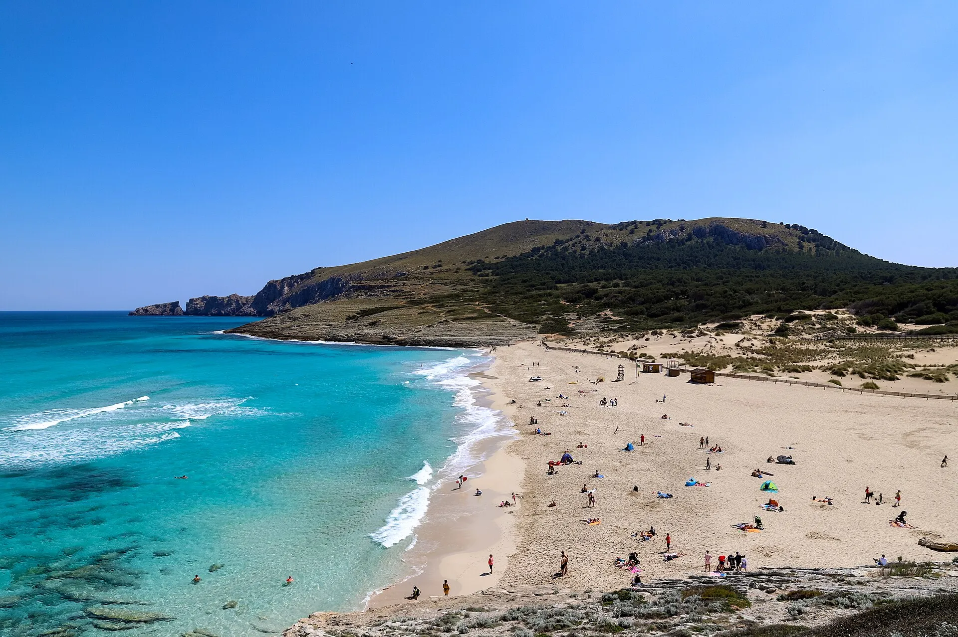 Arena de Cala Mesquida con bañistas y agua turquesa, con el monte del lado este al fondo