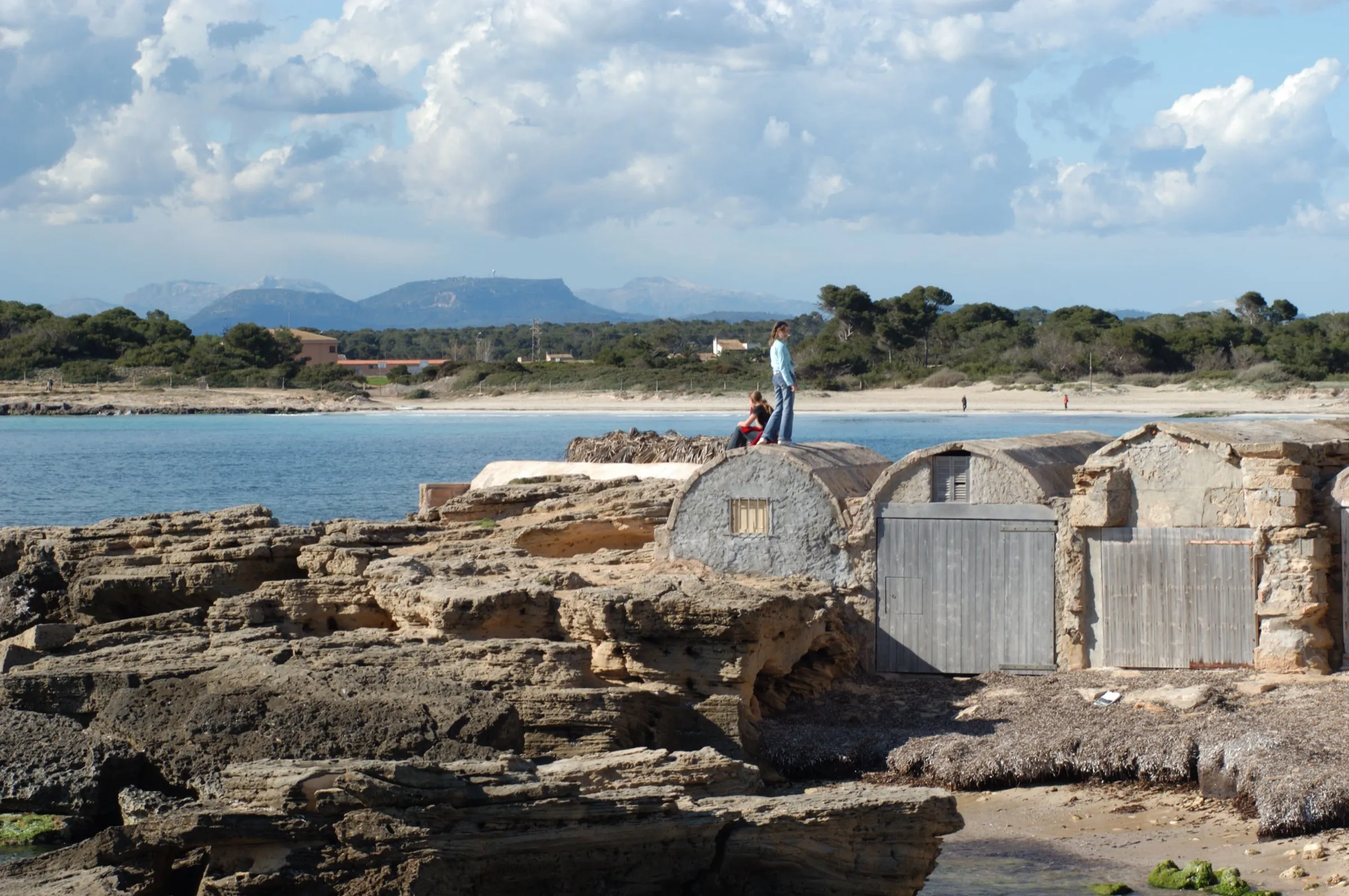 The rock-built boat sheds of es Dolç, with the white sandy beach, the pine woods and the mountains behind