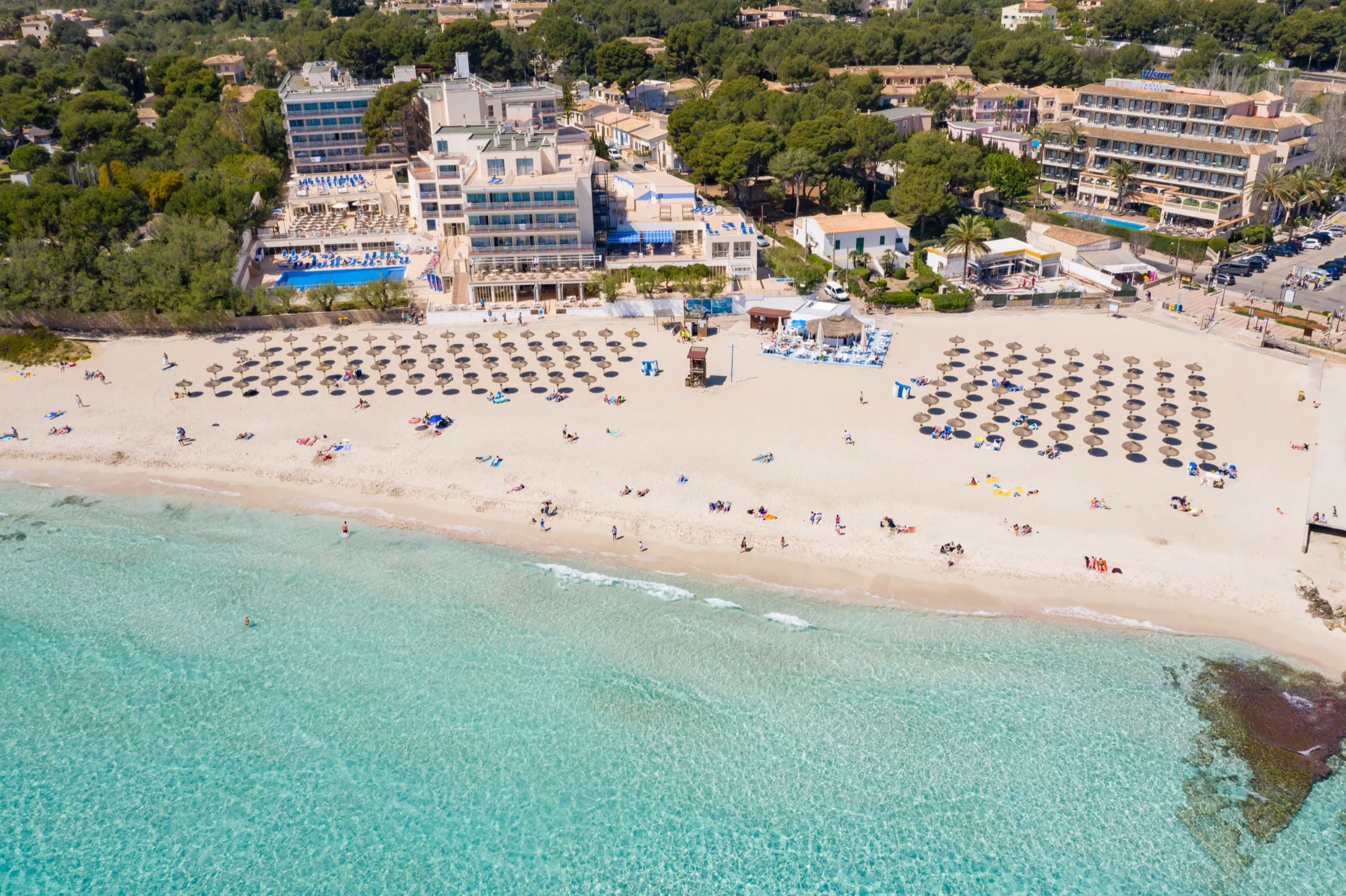 Vista aérea de Son Moll, con la arena clara llena de sombrillas, el agua turquesa y los hoteles detrás