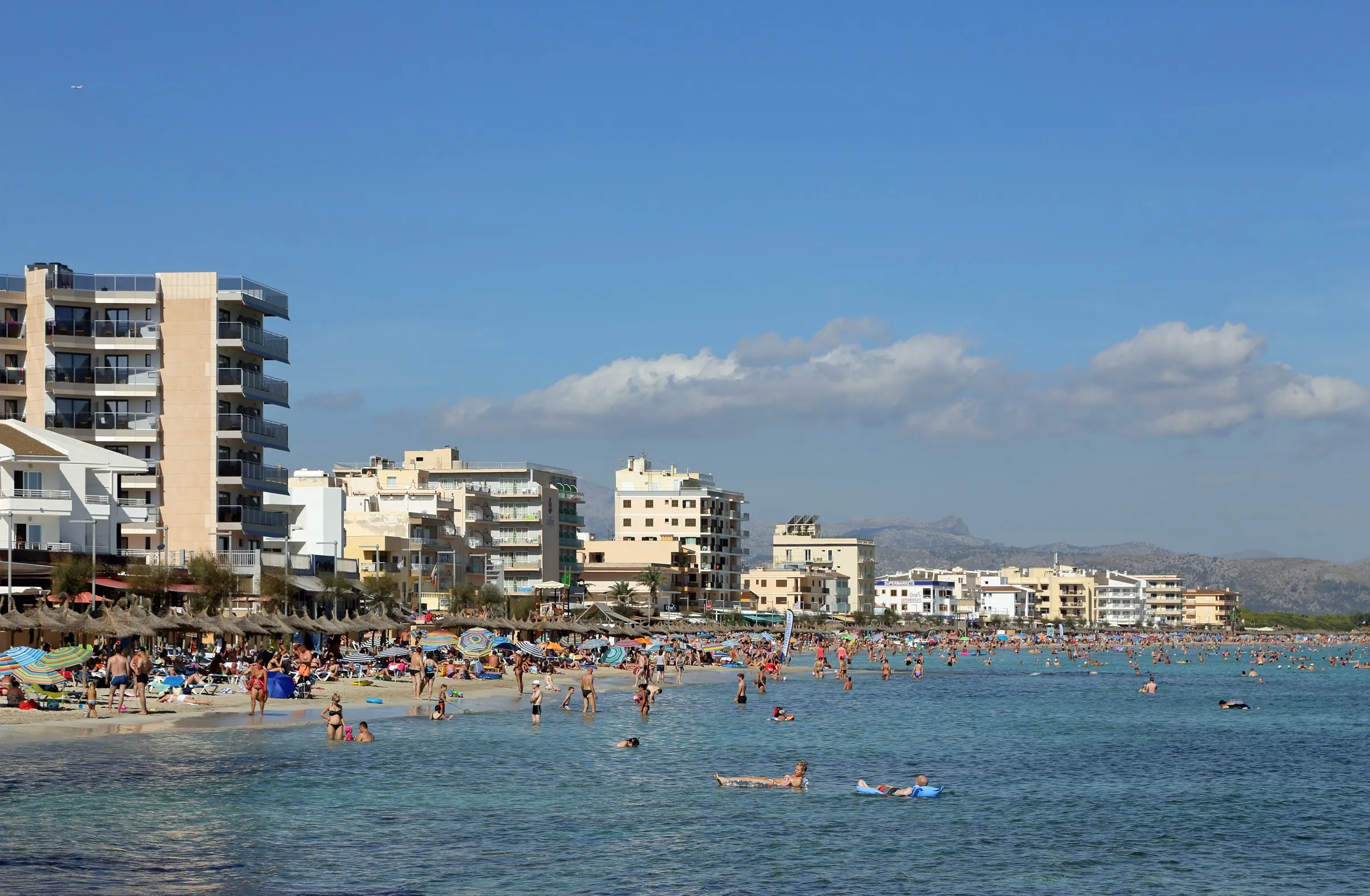 Can Picafort beach with swimmers in the shallow water and the seafront buildings behind