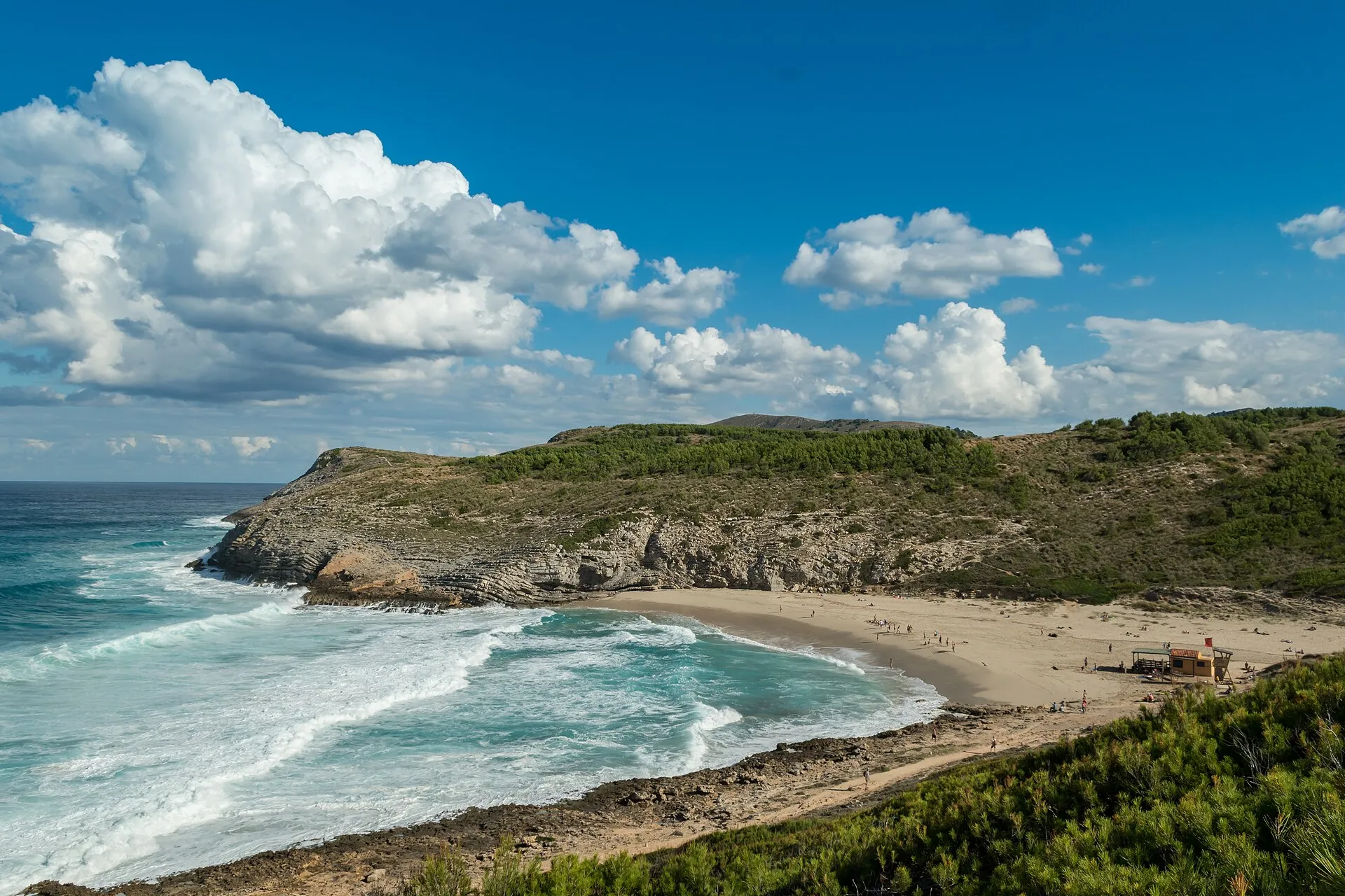 Cala Torta vista desde el monte, con olas entrando en la arena y la punta rocosa del lado oeste
