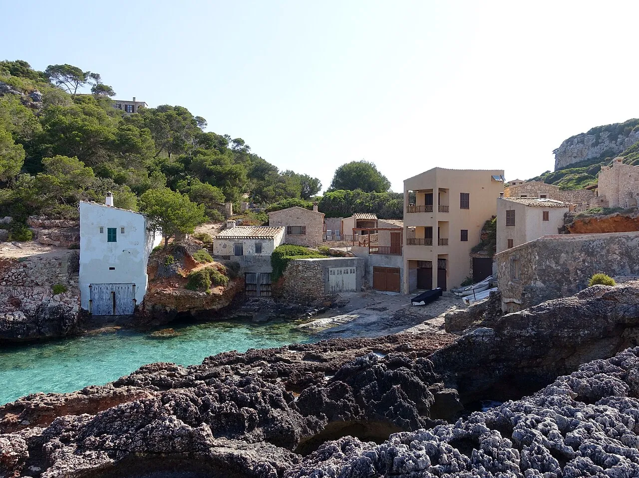 Casas y casetas de pescadores al fondo de Cala s'Almunia, con una caseta blanca junto al agua