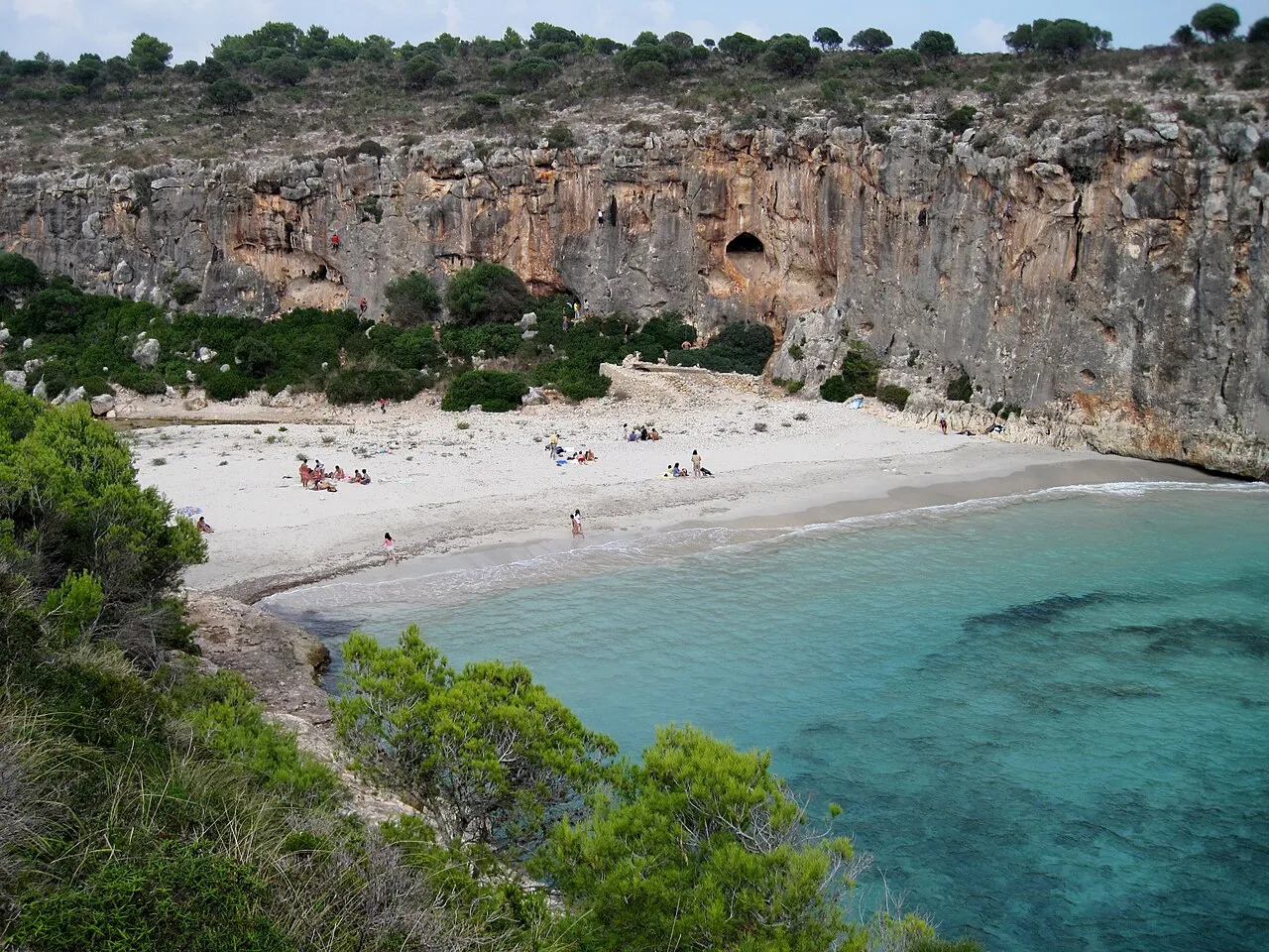 Arena blanca y agua turquesa de Cala Magraner al pie de una gran pared de roca caliza