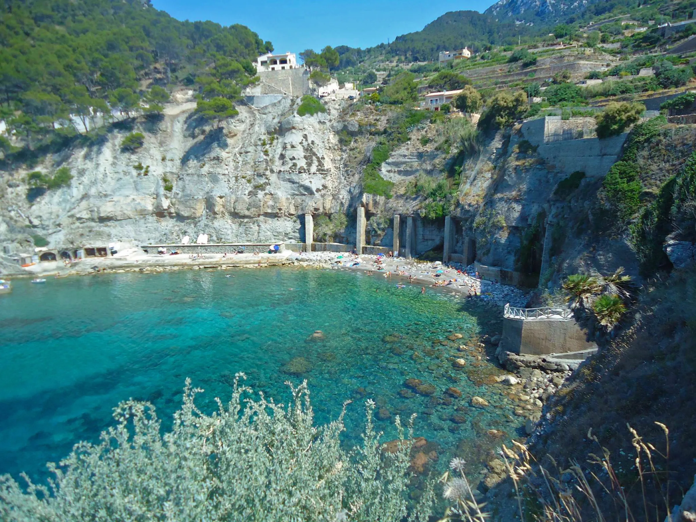 The cove of Banyalbufar from the path, with the rocky bottom under the clear water and the terraces on the slope