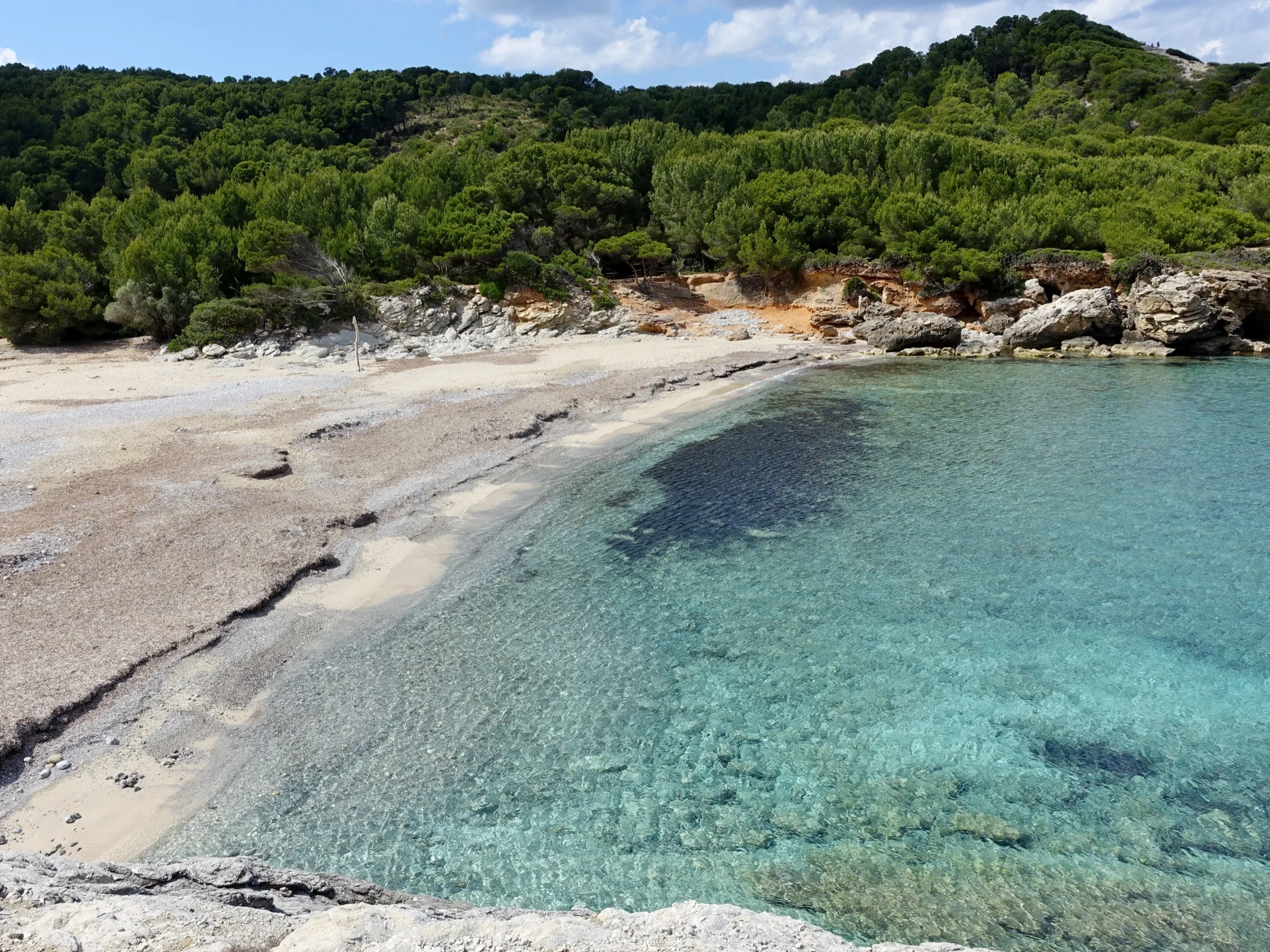 Agua turquesa y transparente sobre la arena en la orilla de Cala Matzoc