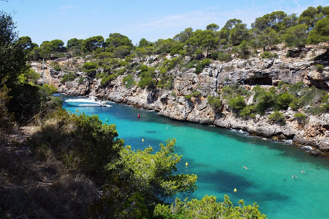 El entrante de Cala Pi entre paredes de roca y pinar, con boyas de balizamiento y una lancha fondeada