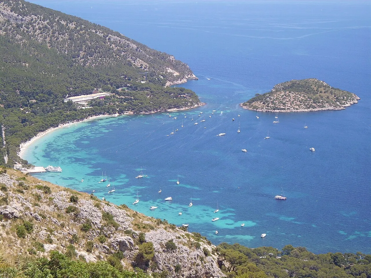 La playa de Formentor desde la Talaia d'Albercutx, con el hotel, el embarcadero, los barcos fondeados y la Illa de Formentor