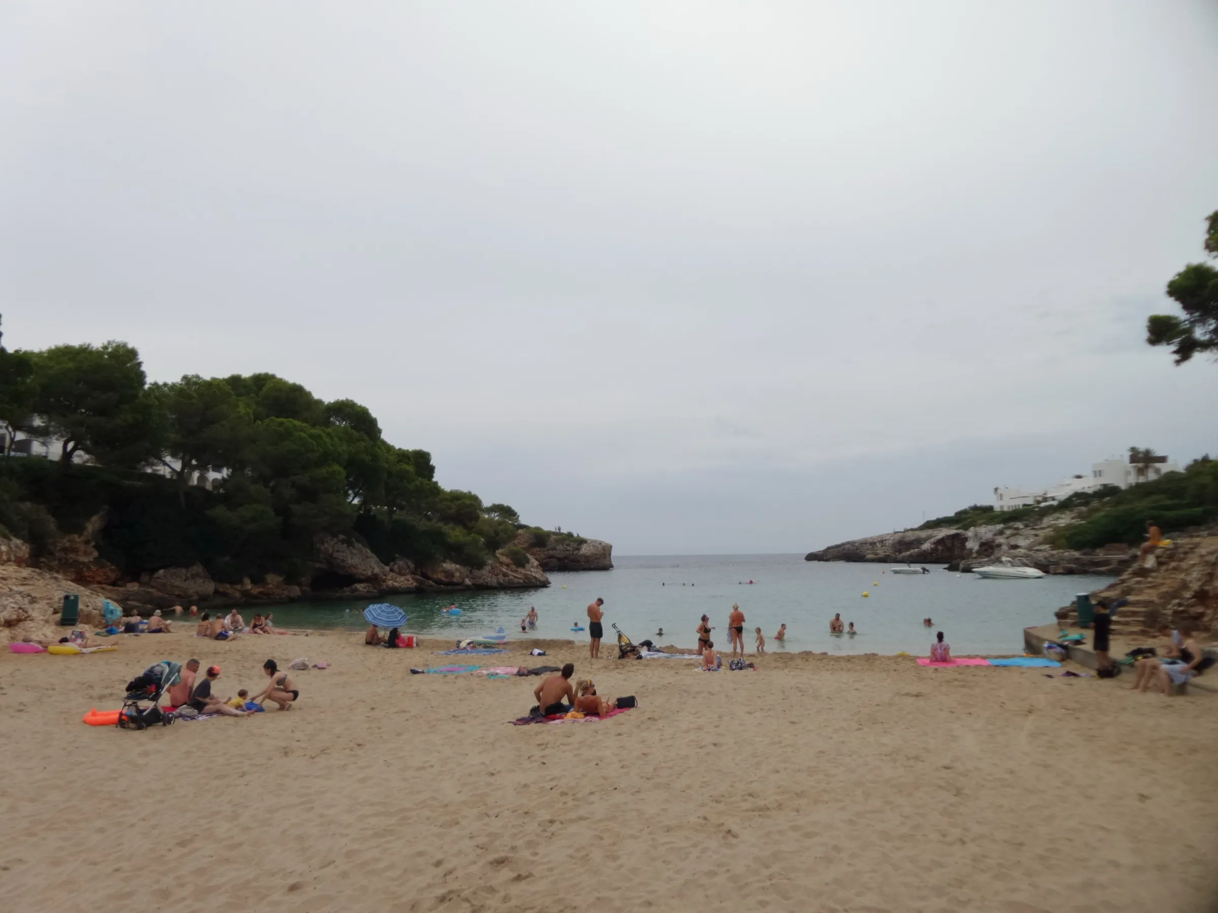 La arena de Cala Esmeralda con toallas y bañistas, y el entrante de mar que sale entre dos laderas de pinos