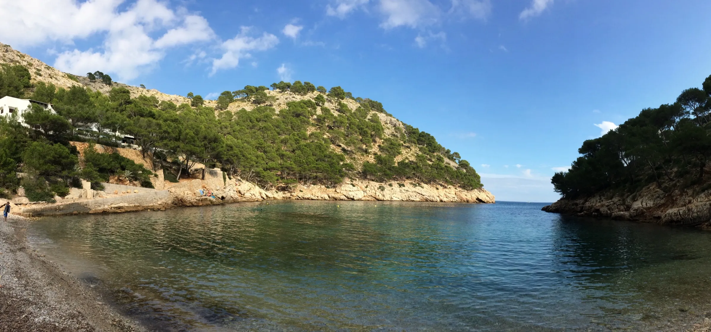 Playa de cantos de Cala Murta con una casa blanca entre los pinos de la ladera