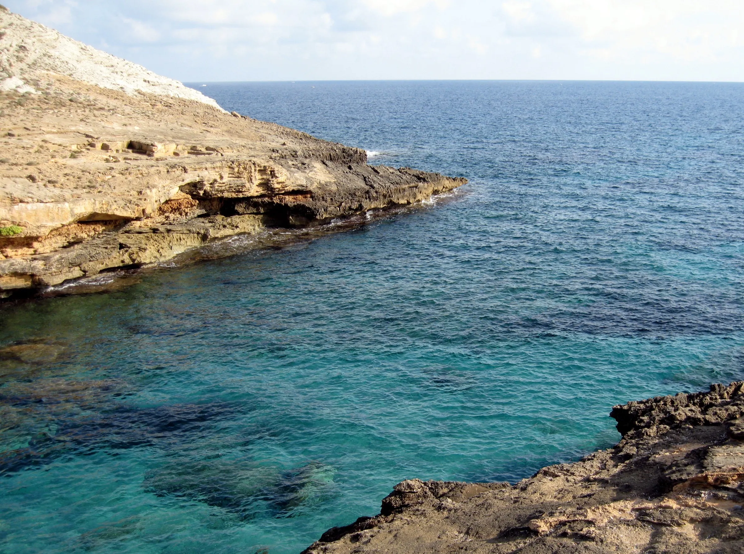 Agua turquesa en la boca de Cala Estreta, junto a una punta de roca clara