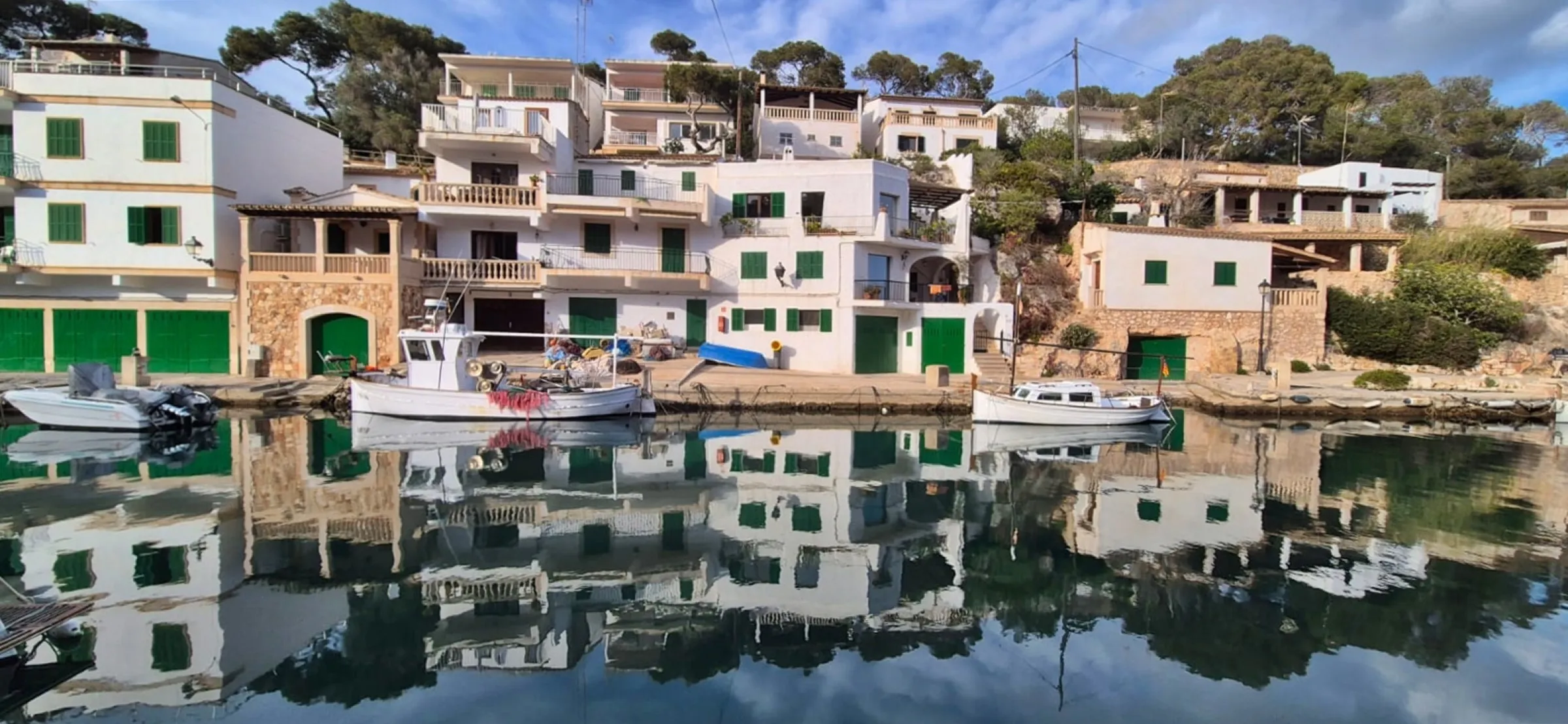 Weiße Fischerhäuschen mit grünen Toren und Booten, die sich im Hafenwasser spiegeln