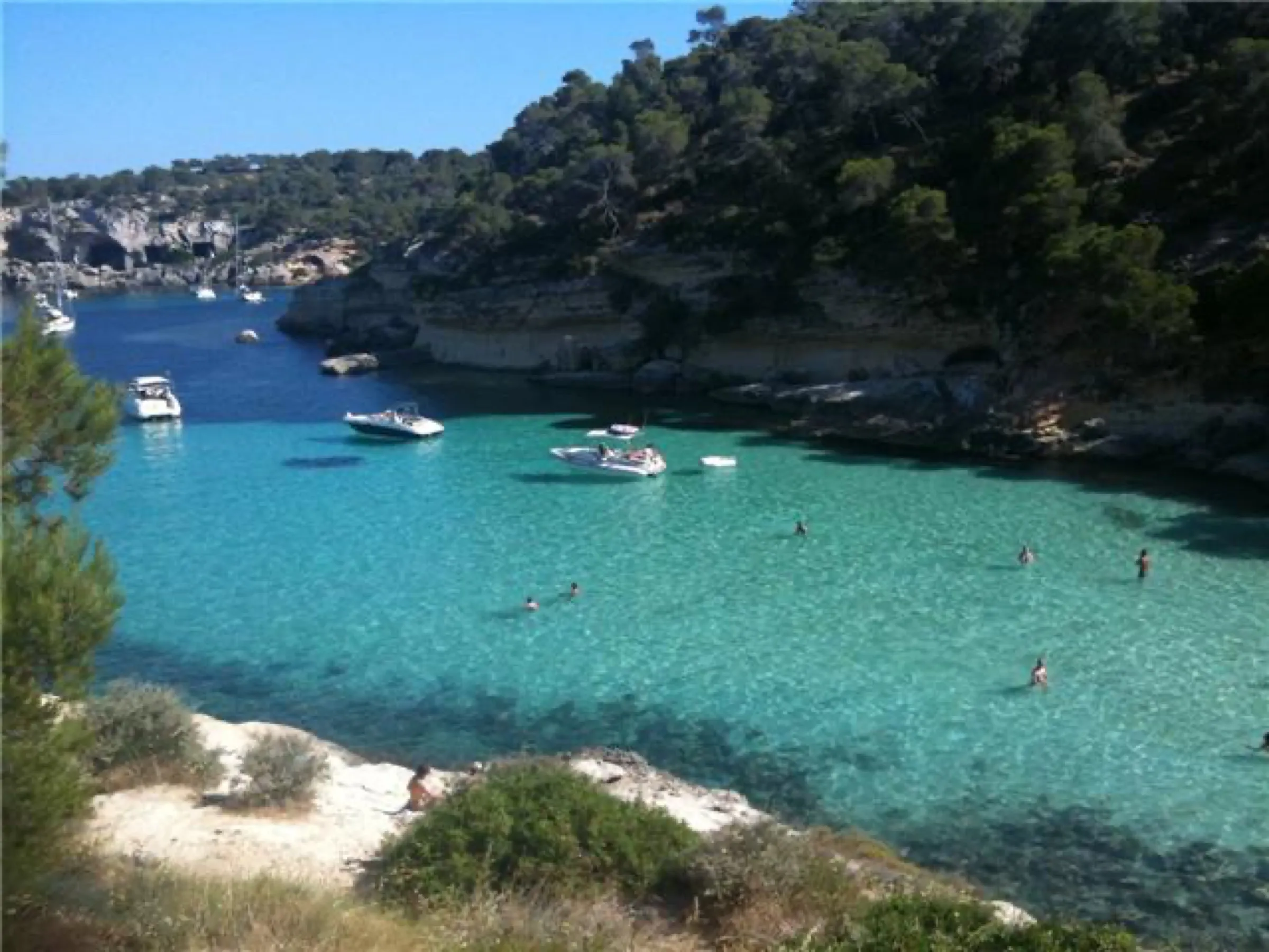 Bañistas y barcos fondeados en el agua turquesa frente a la Platja des Mago