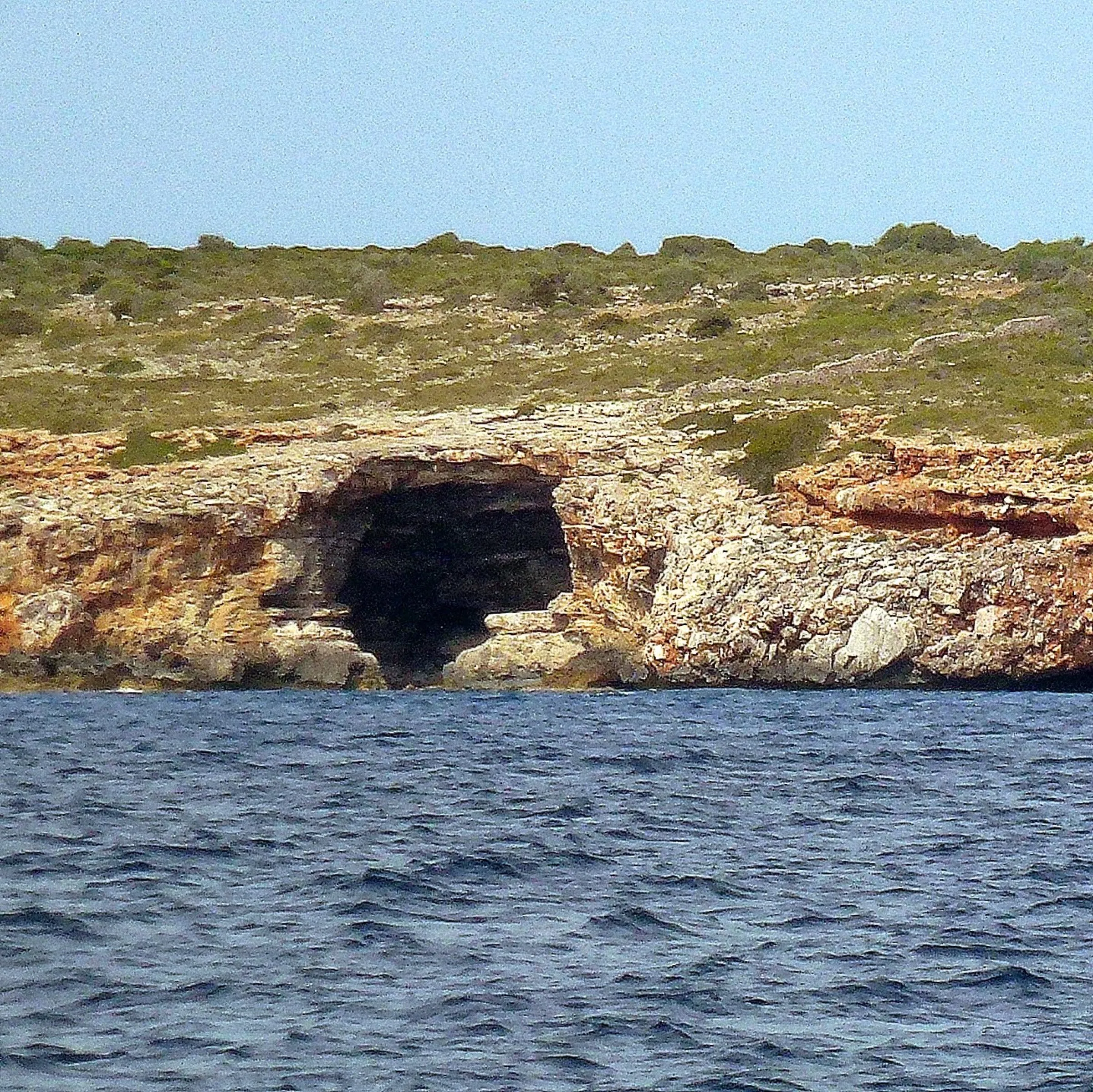 Acantilados de roca con cuevas junto al mar en la costa cercana al Caló des Màrmols, vistos desde el agua