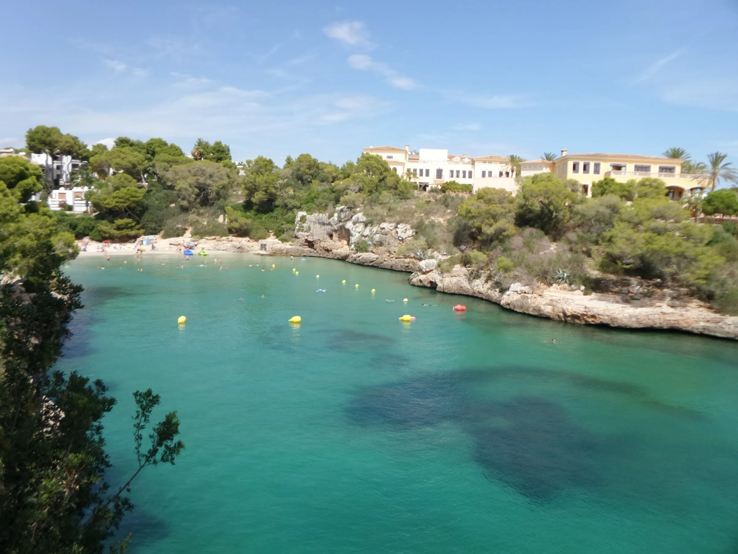 Cala Ferrera vista desde lo alto, con el agua verde clara, la arena al fondo y las casas entre el pinar