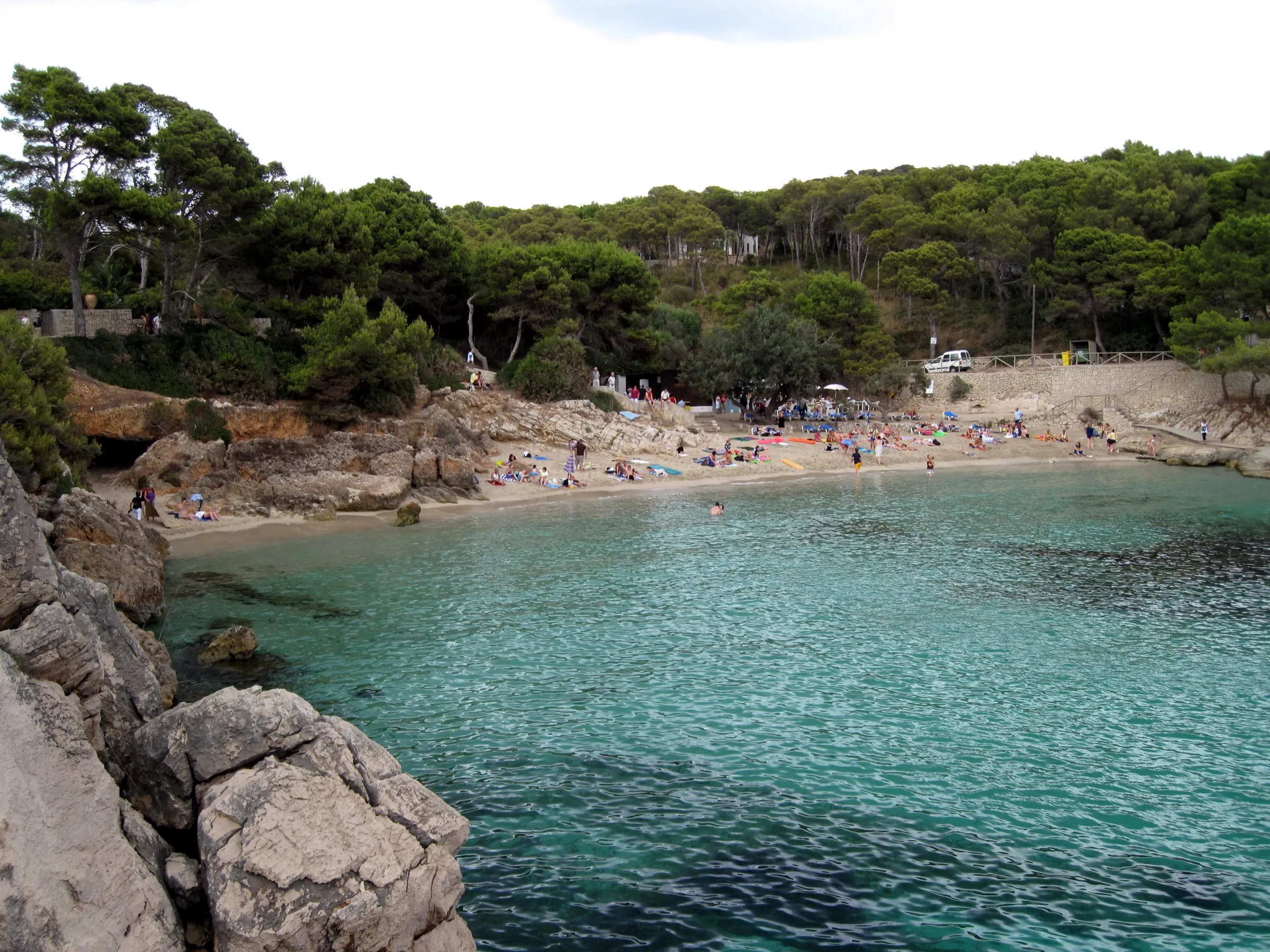 Vista de Cala Gat desde las rocas, con el agua verde clara y la playa al fondo bajo el pinar