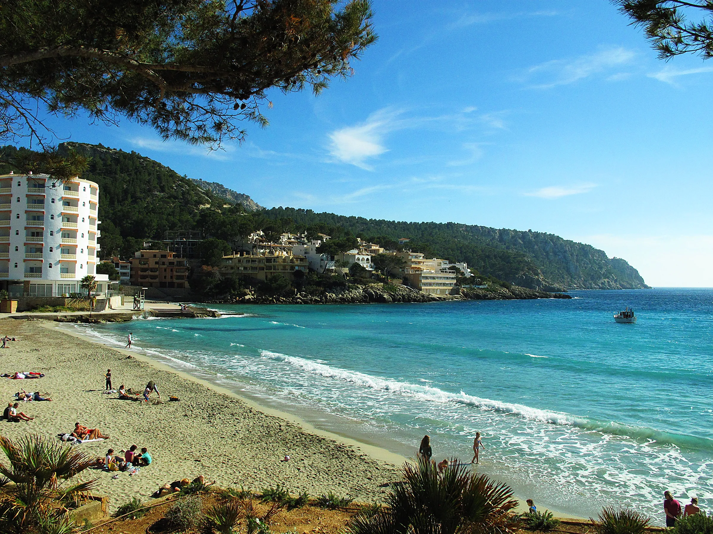 Arena de la playa de Sant Elm con bañistas y, al fondo, la costa acantilada hacia la punta de s'Estaca