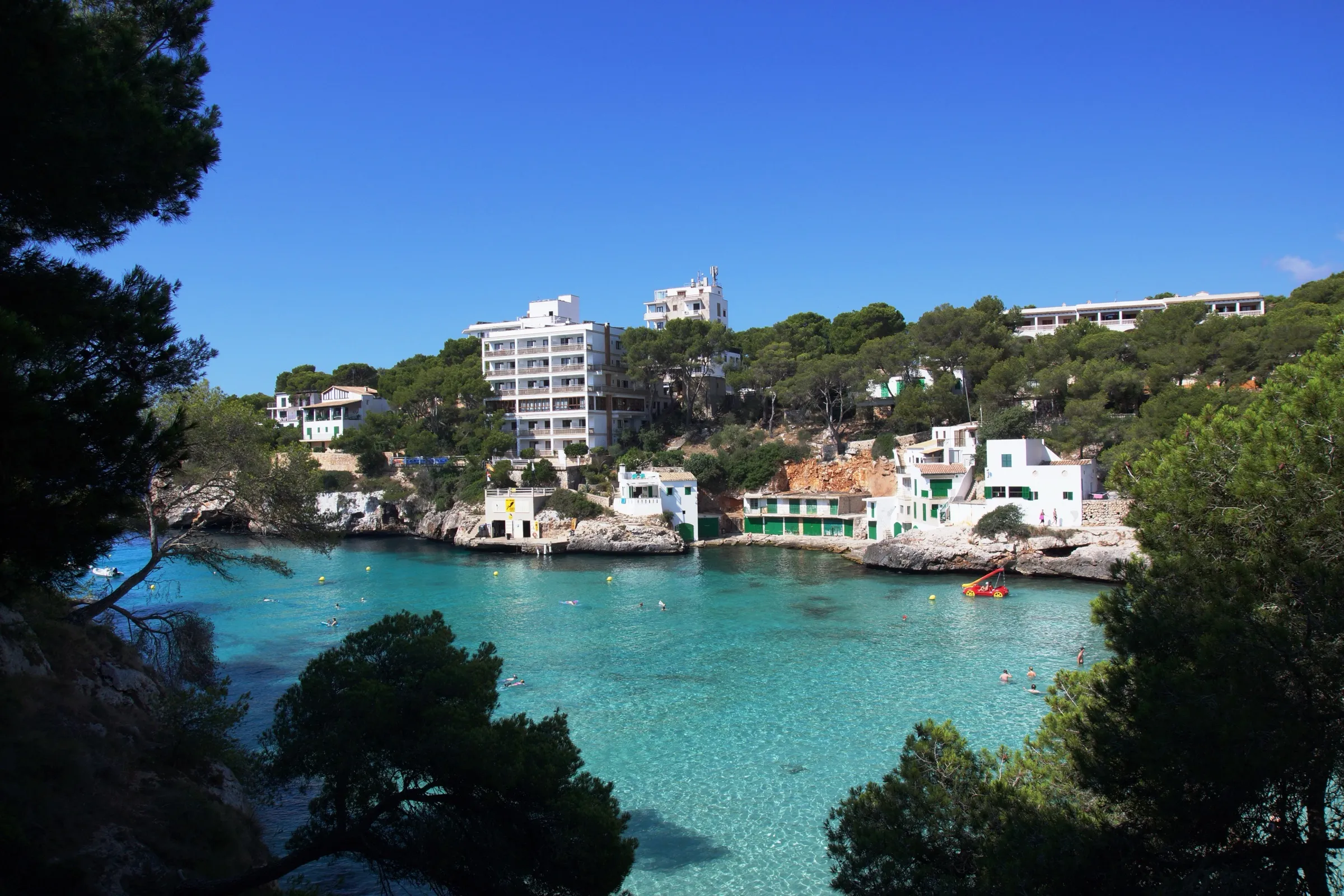 El entrante de Cala Santanyí desde lo alto, con el agua verde azulada entre pinos y las casetas de pescadores en la orilla
