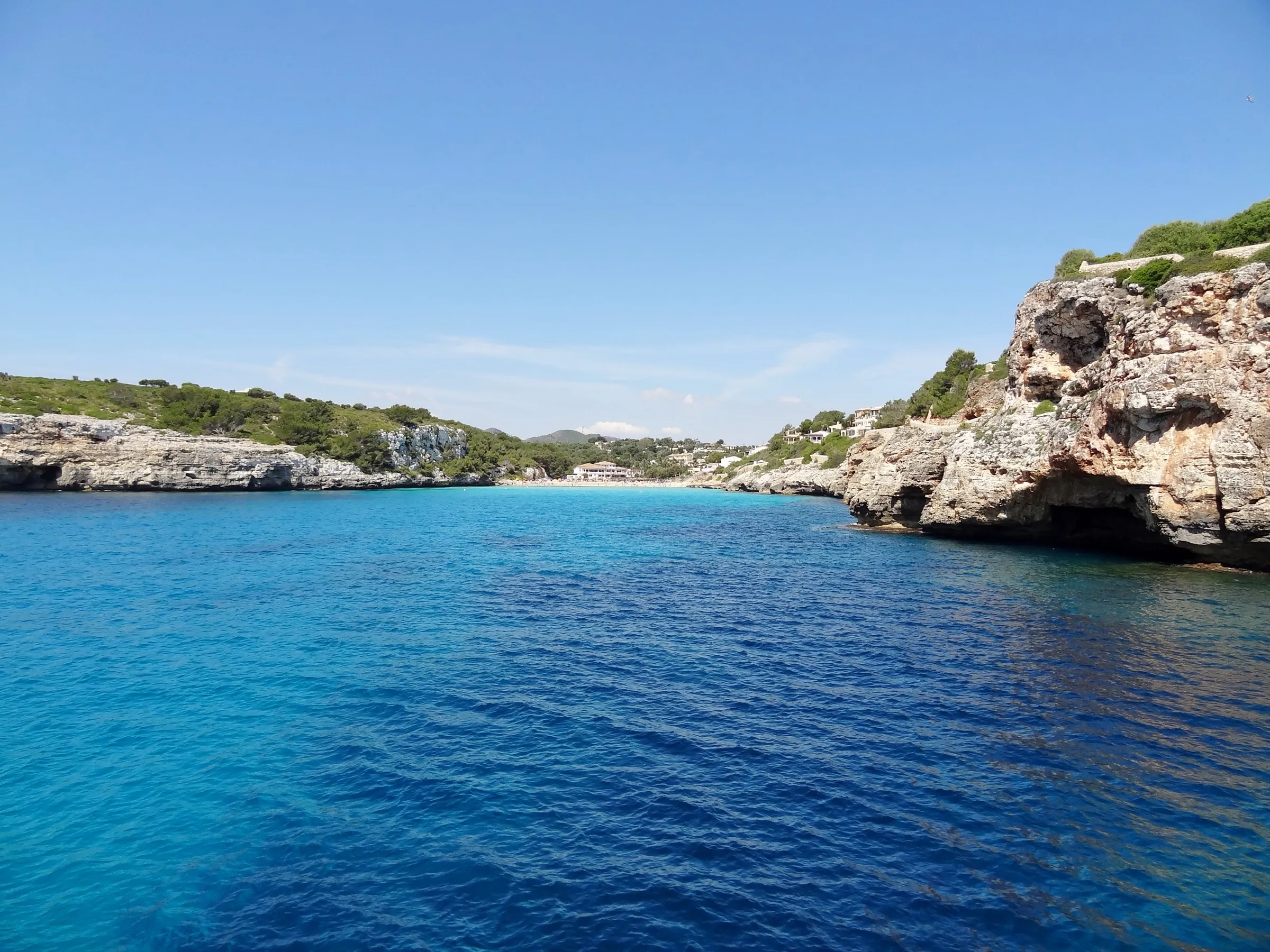 La cala vista desde el mar, estrecha y larga entre paredes de roca caliza, con la playa al fondo