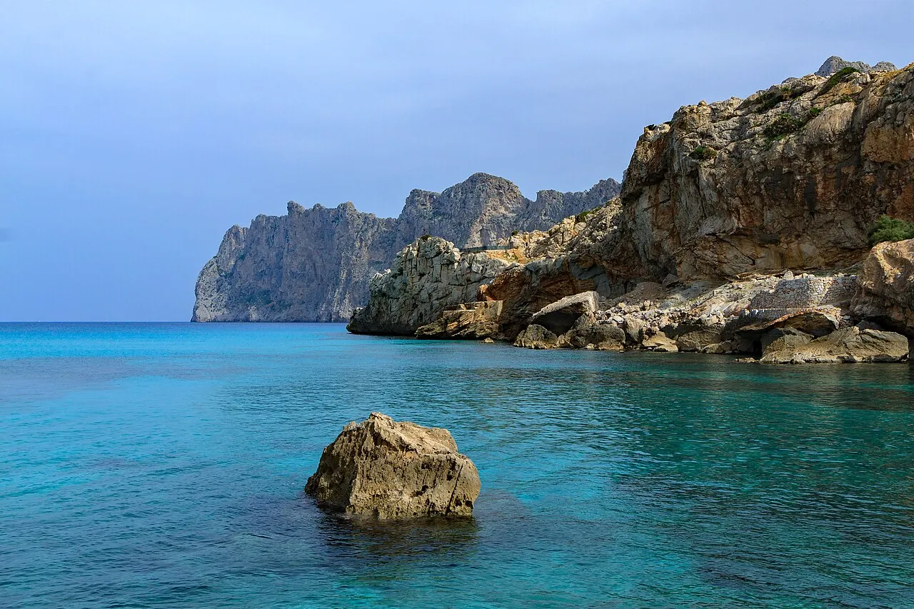 Agua turquesa de Cala Barques con una roca aislada y los acantilados del Cavall Bernat al fondo