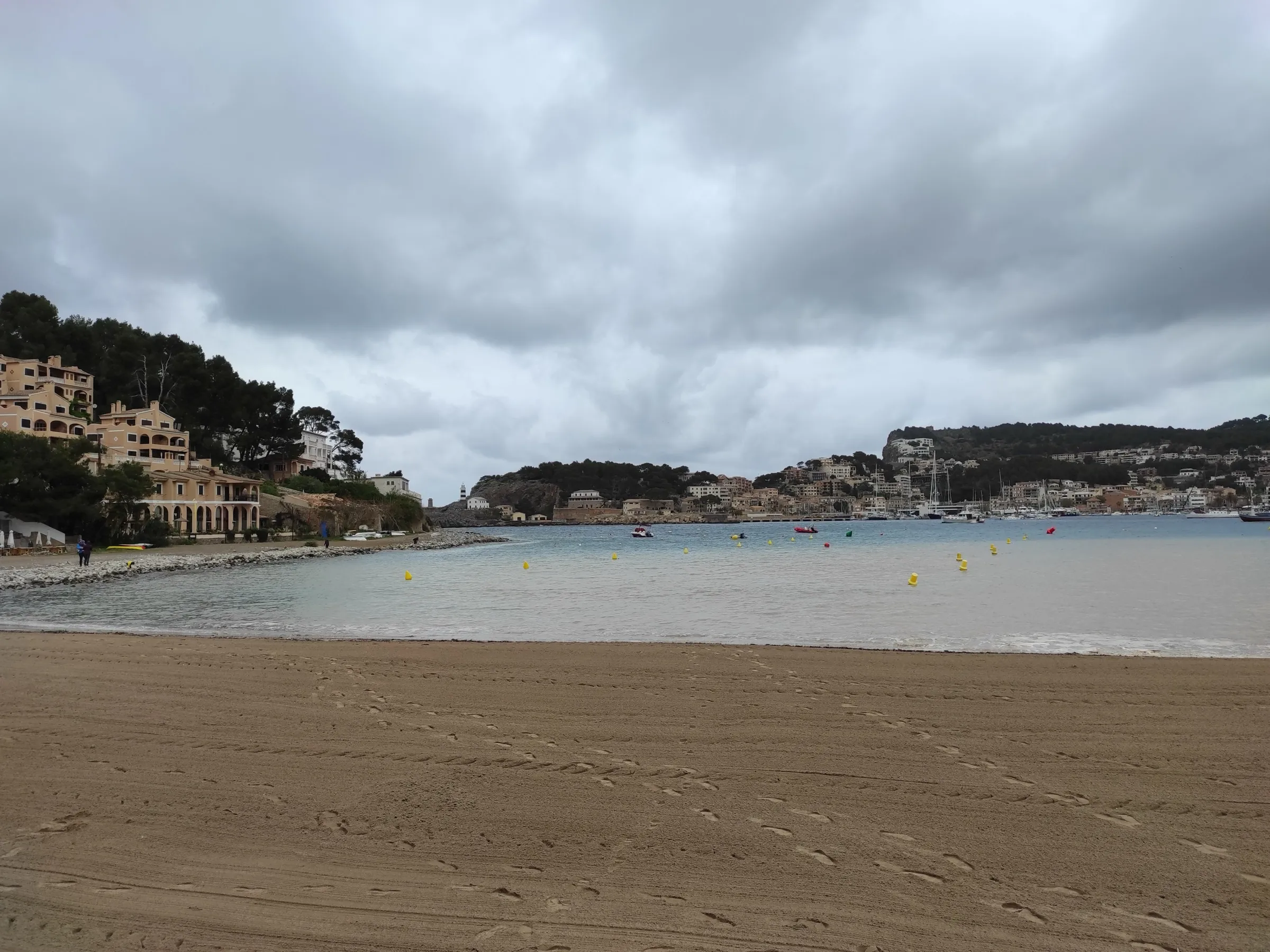 Platja d'en Repic en un día nublado, con la arena vacía, las boyas en el agua y los hoteles de la ladera a la izquierda