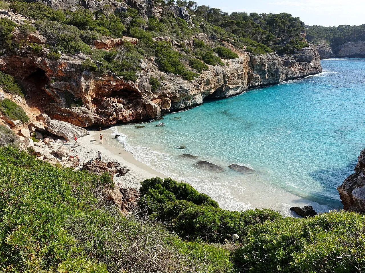 Arena blanca y agua clara al fondo del Caló des Moro, entre paredes de roca