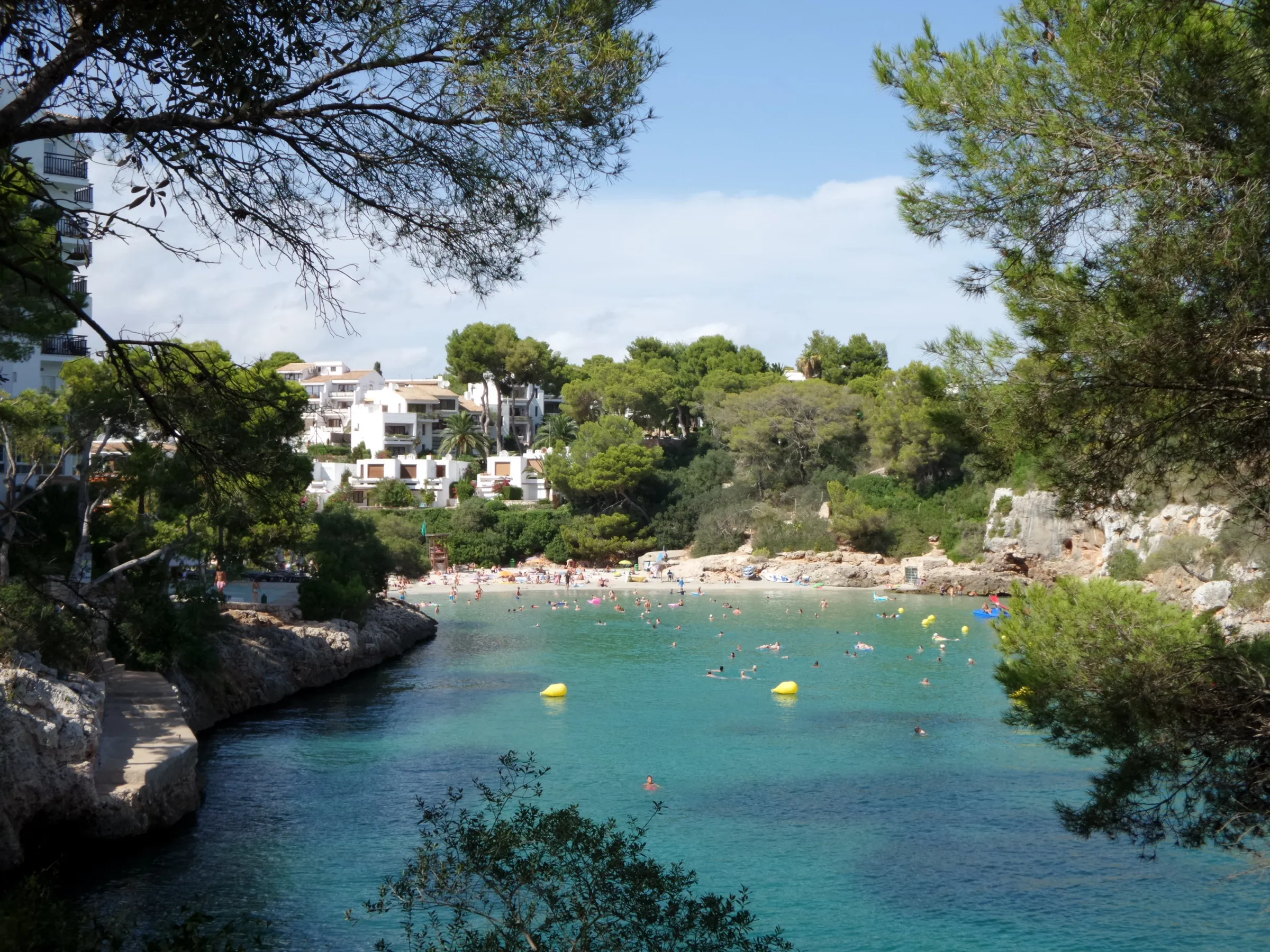 La playa de Cala Ferrera vista entre los pinos, con el agua clara y las rocas de la orilla
