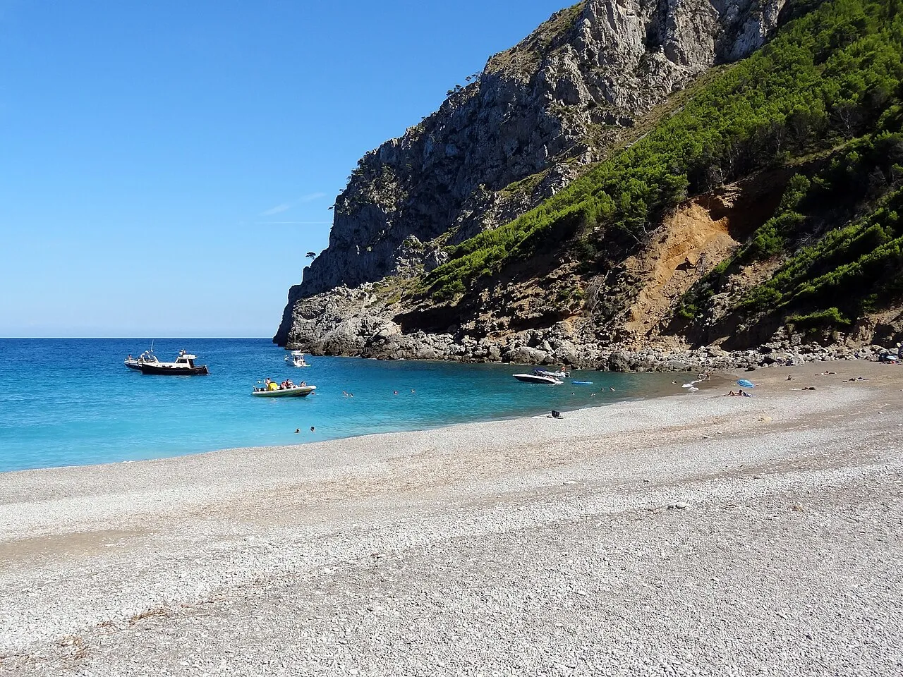 Barcas fondeadas frente a la playa de es Coll Baix, bajo una ladera de pinar y roca