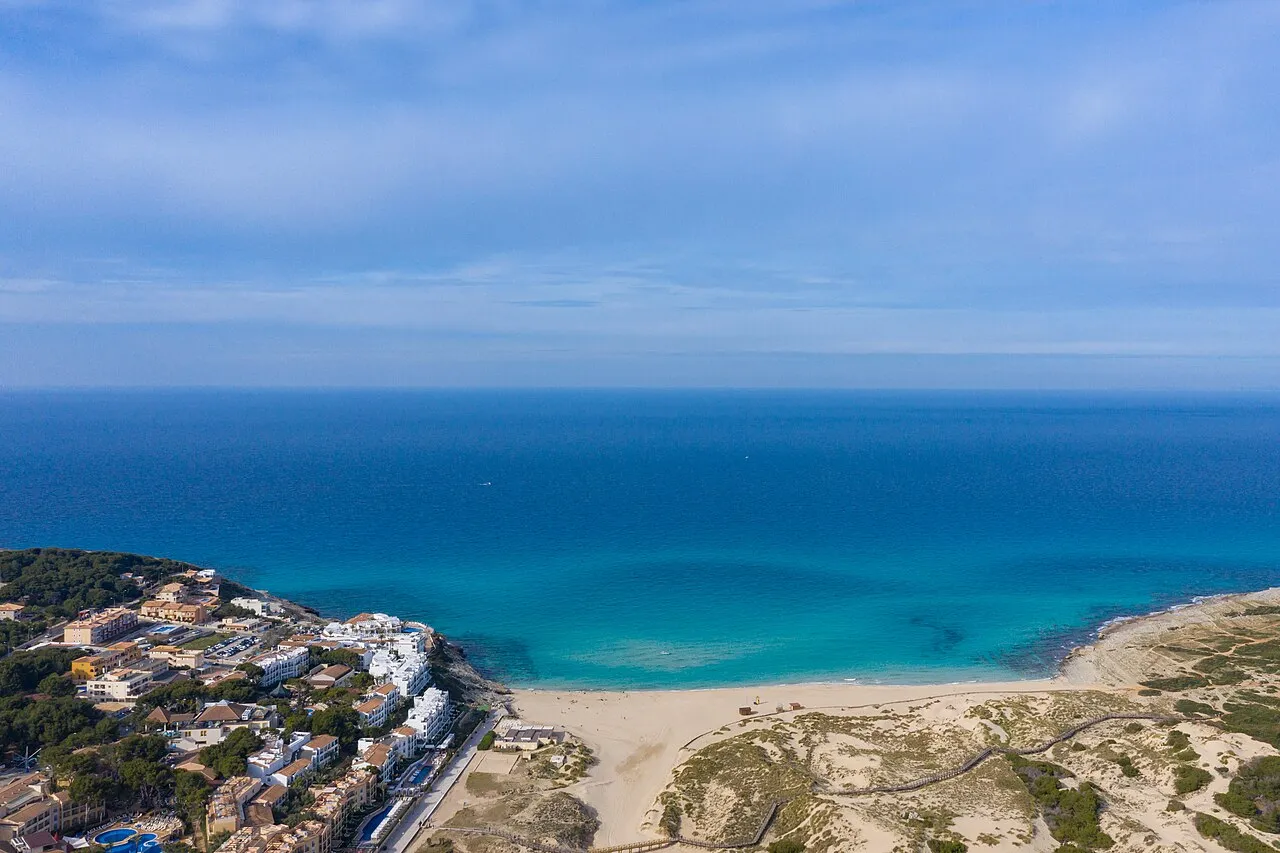 La playa vista desde el aire, entre la urbanización y las dunas, con el mar abierto detrás