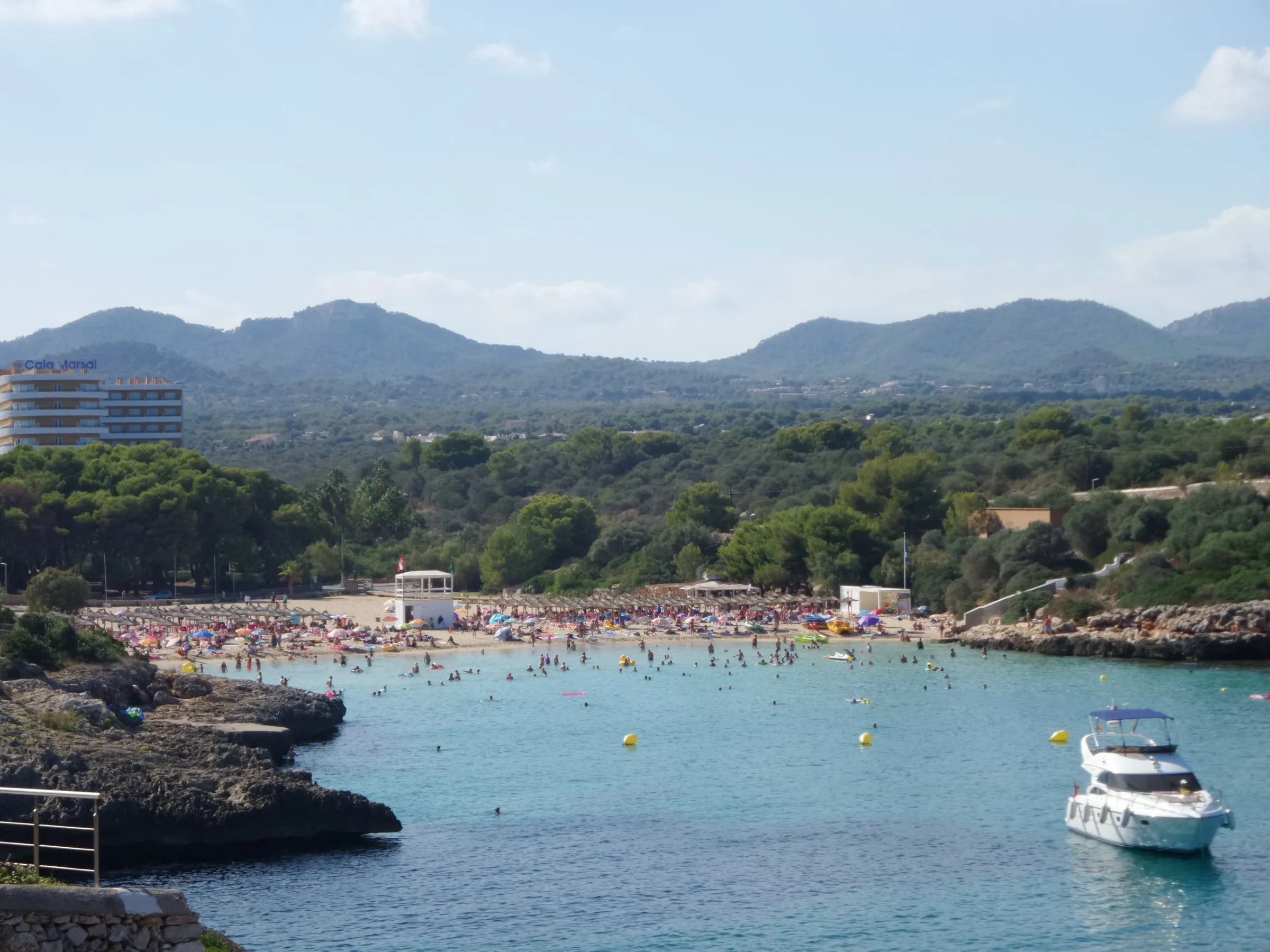 Una lancha fondeada en el agua azul de Cala Marçal, con la playa, el pinar y las montañas al fondo