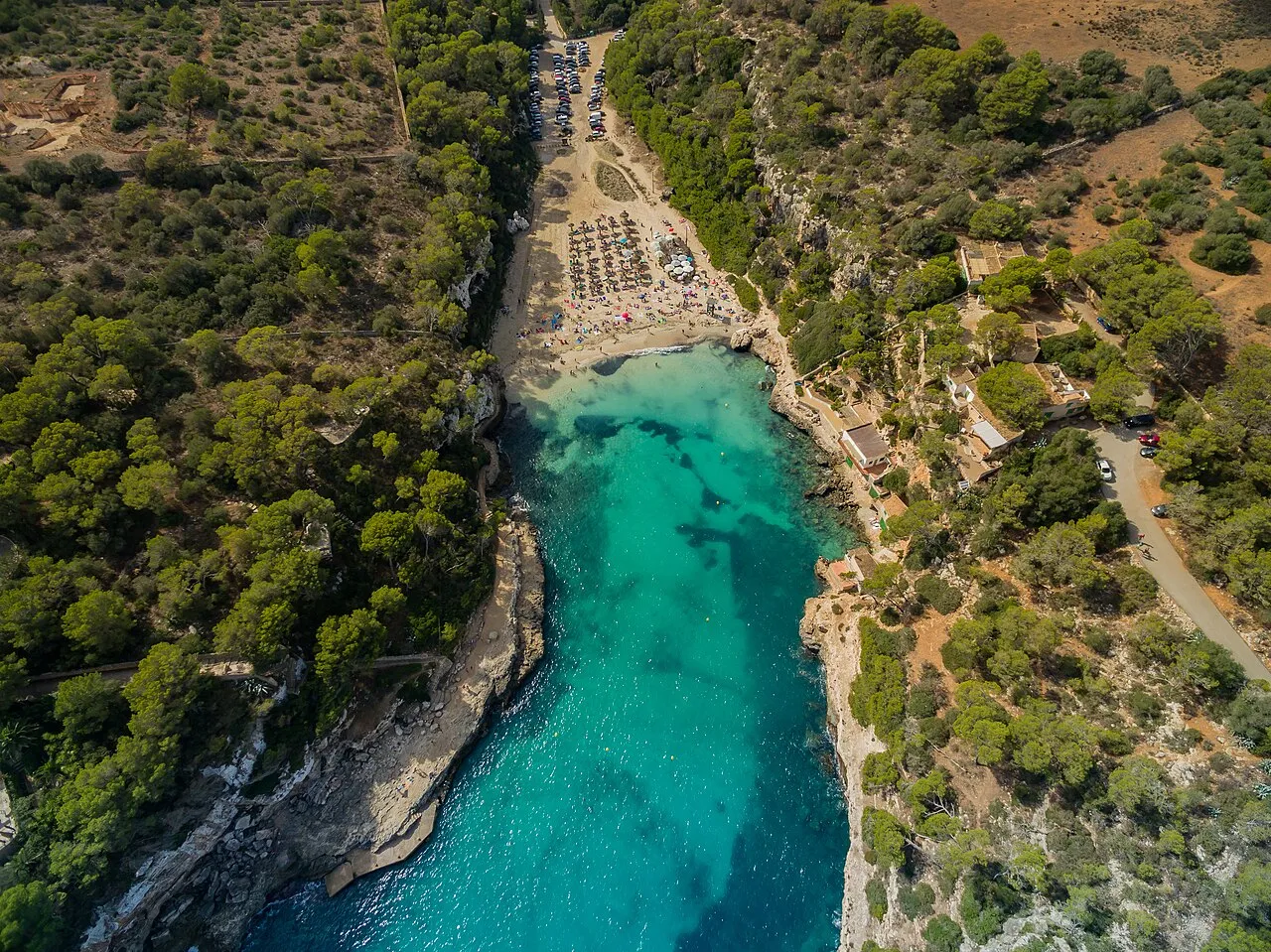 Vista aérea cenital de Cala Llombards, un entrante estrecho de agua turquesa que termina en la playa