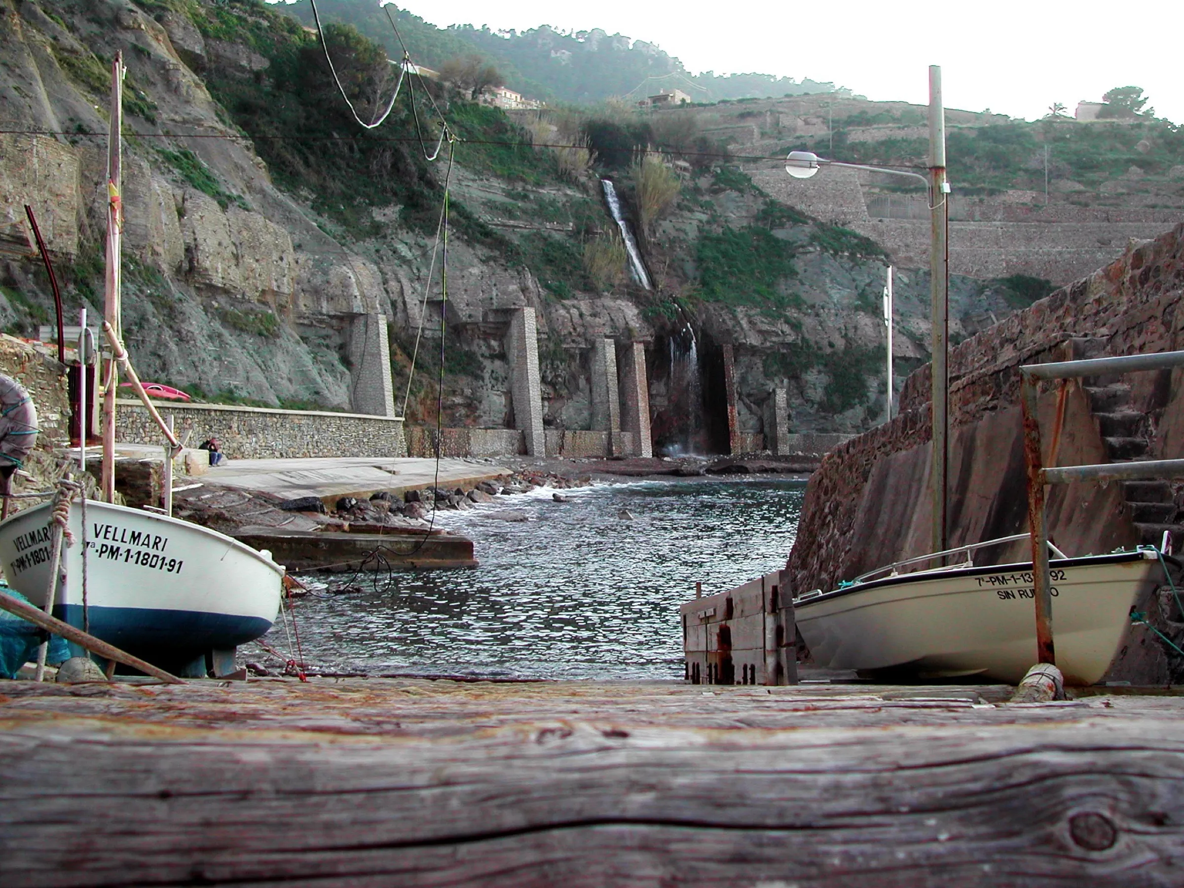 Fishing boats hauled up on the Banyalbufar landing, with the waterfall pouring down the cliff behind