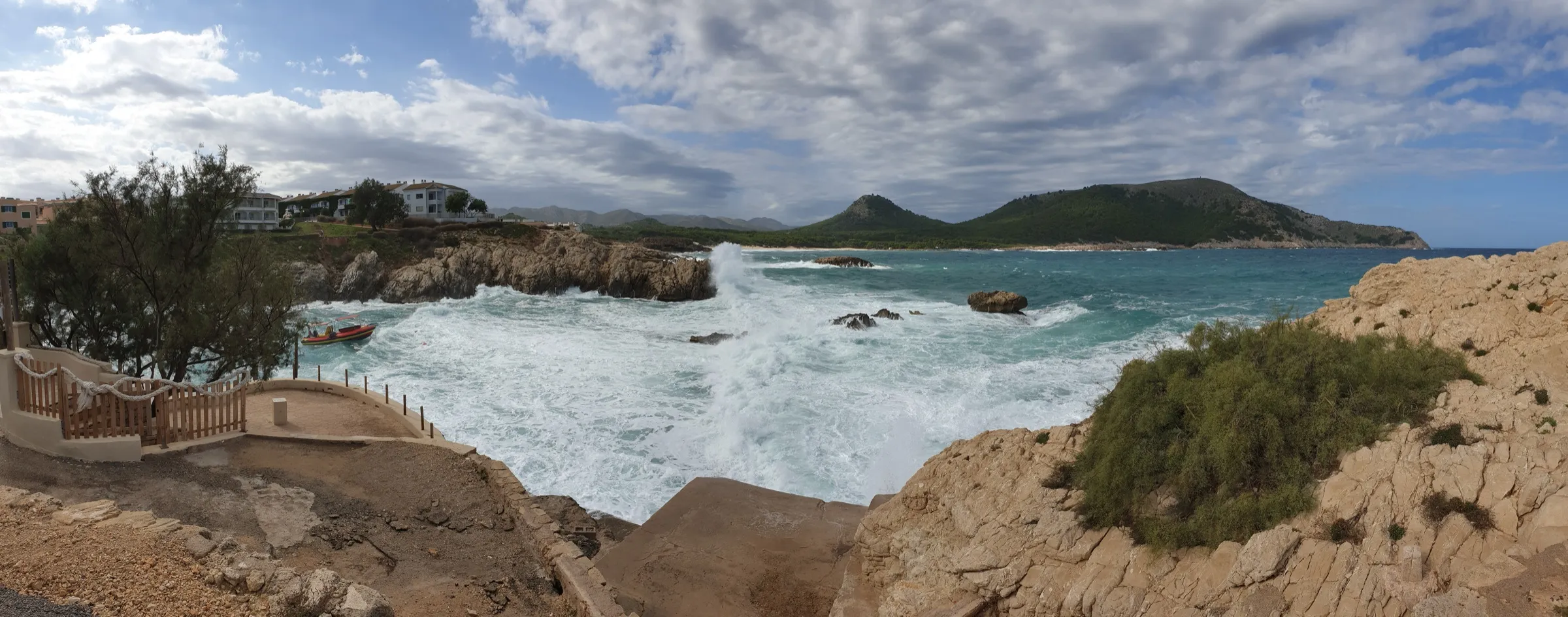 Panorama der Küste an der Cala Lliteres bei Wellengang, mit den Felsen und dem Holzsteg