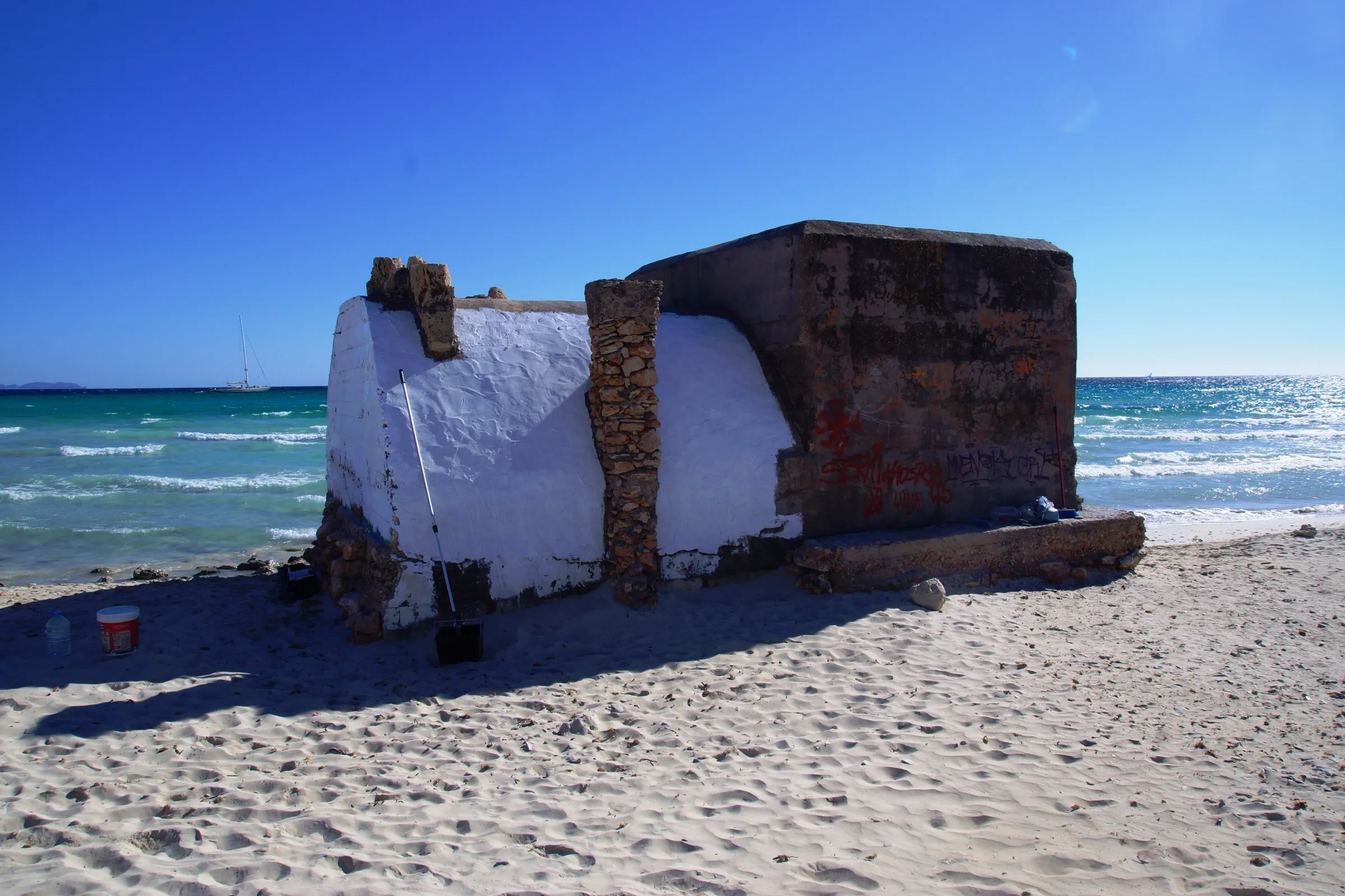 Uno de los búnkeres pintados de blanco sobre la arena del arenal de sa Ràpita, con el mar detrás