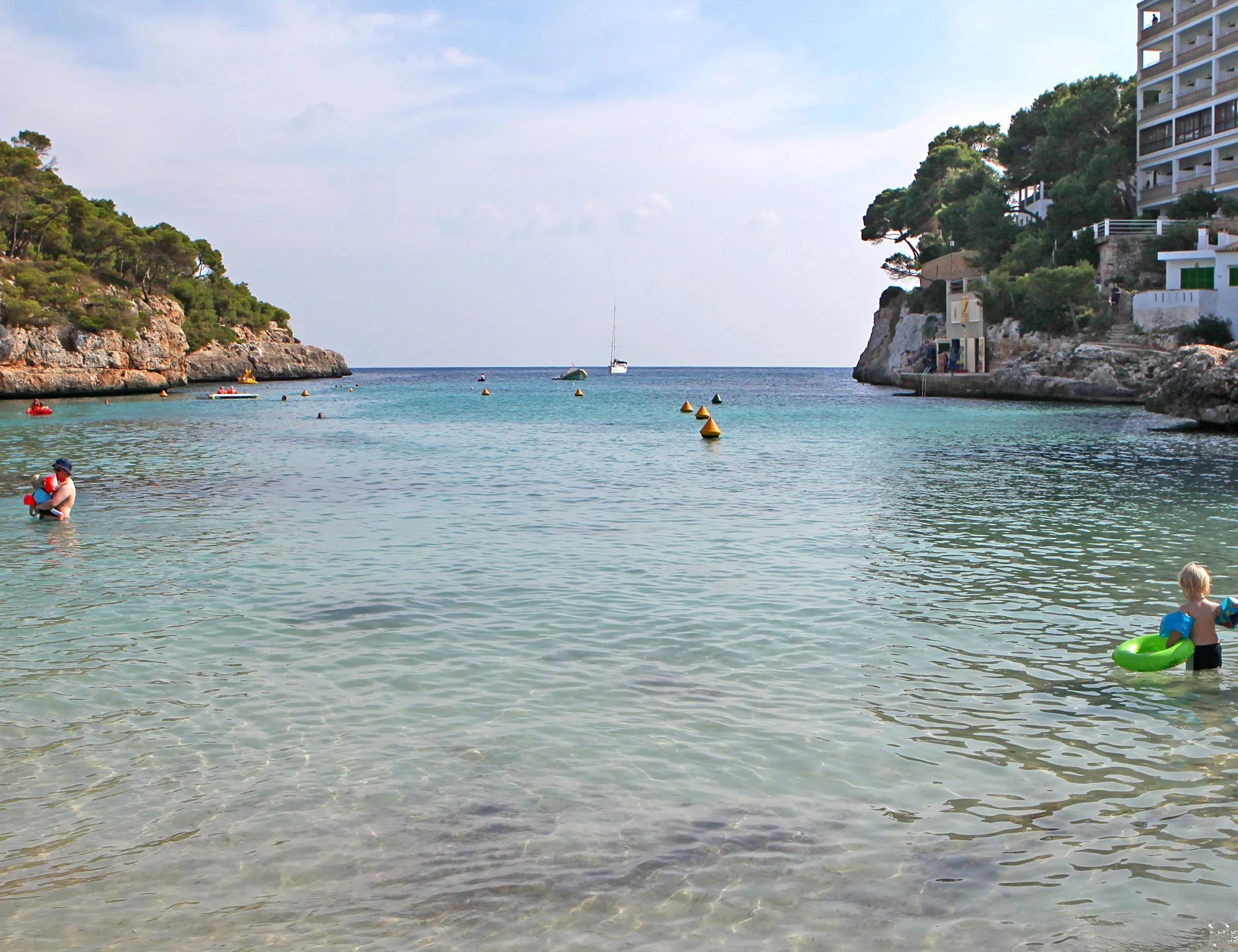 Bañistas en el agua transparente de Cala Santanyí, mirando hacia la boca de la cala entre dos paredes de roca