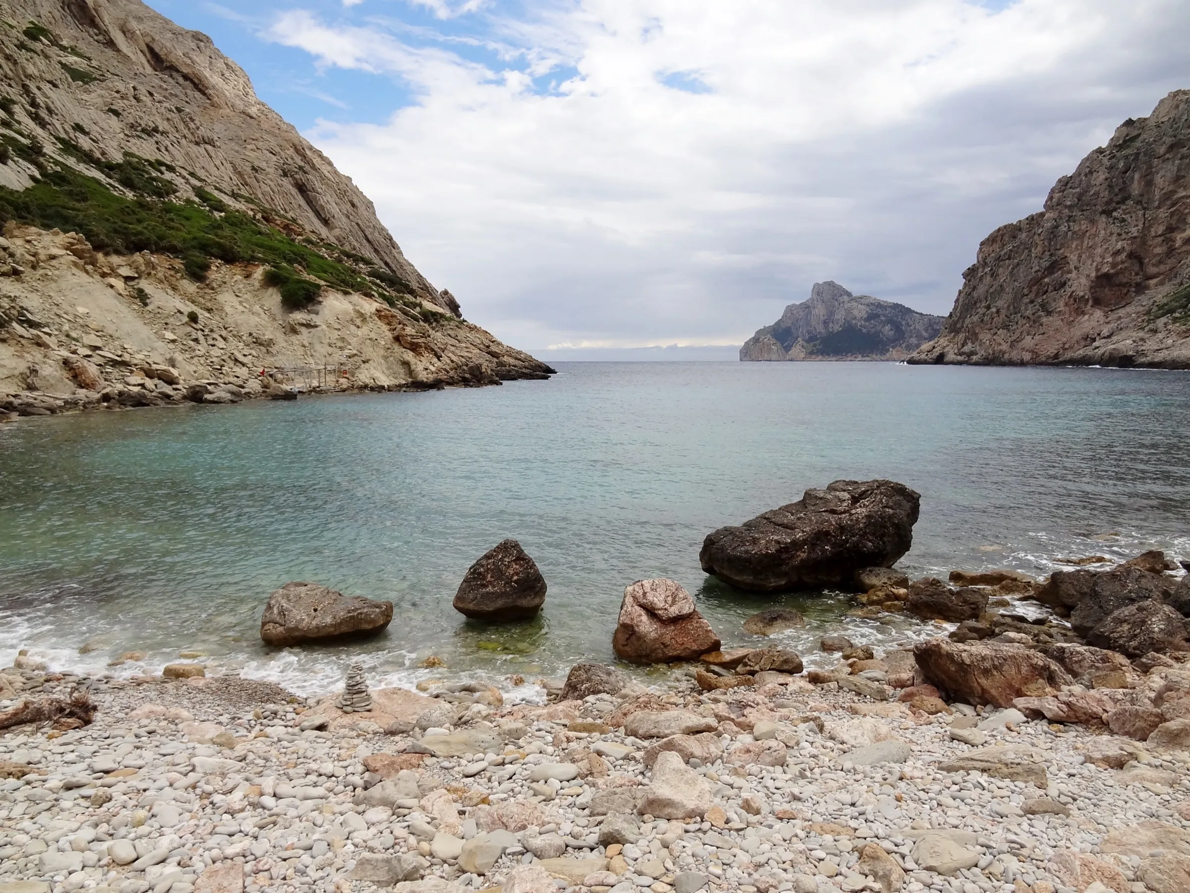 Playa de cantos de Cala Bóquer con grandes rocas en la orilla y las paredes del entrante detrás