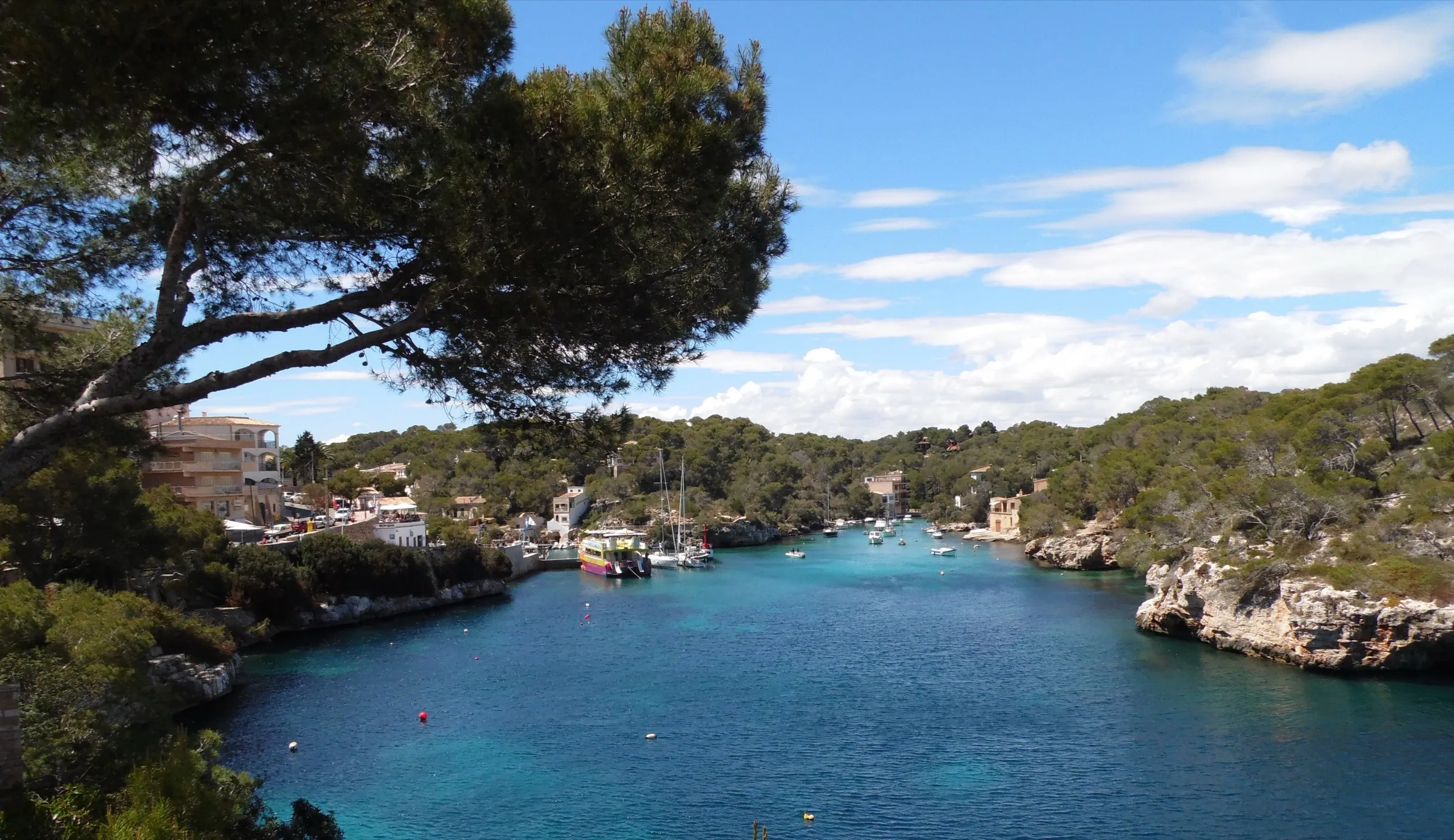 Panorama der Bucht mit blauem Wasser, links das Dorf und rechts niedrige Klippen